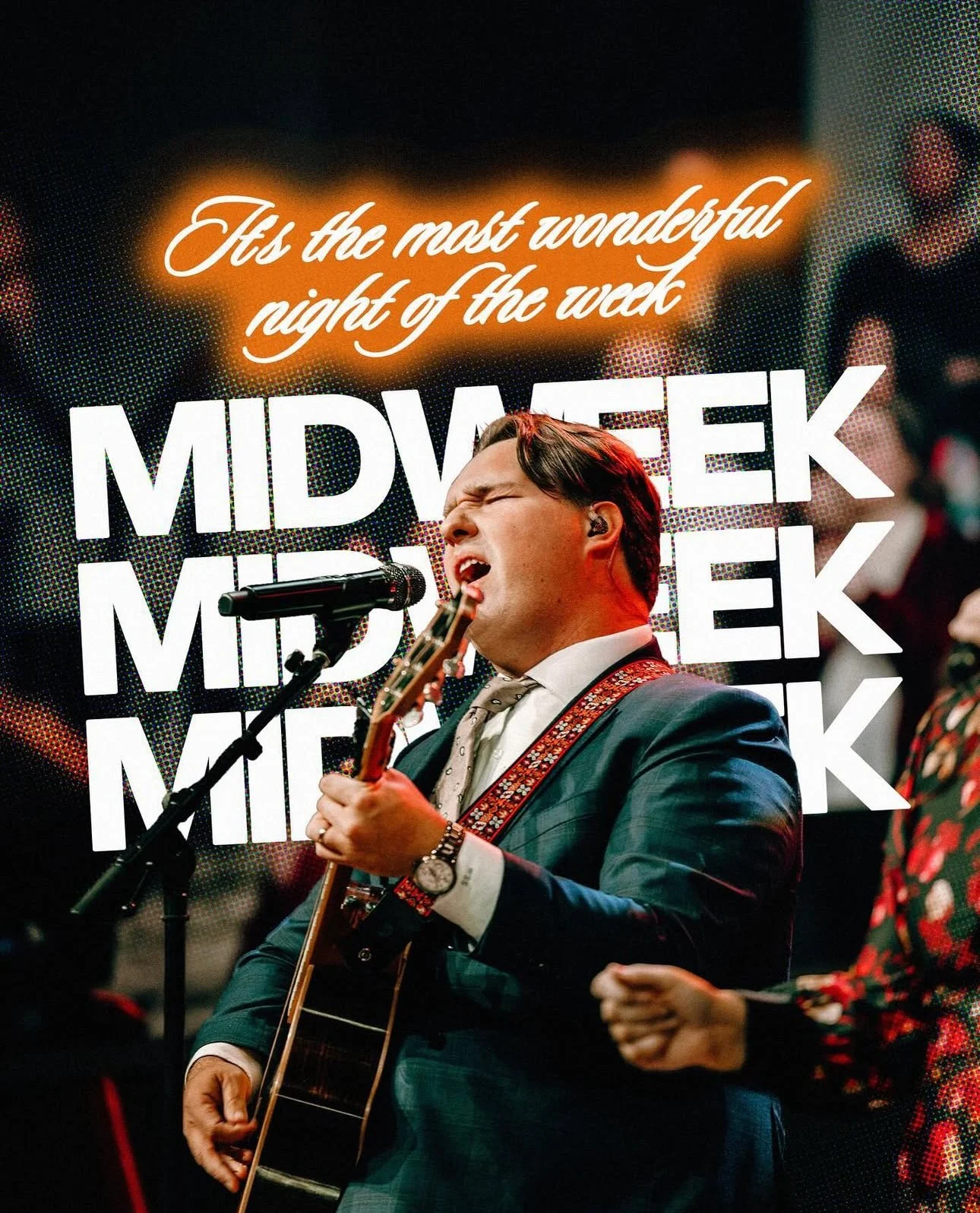 A man singing passionately while playing a guitar on stage during a midweek event, with a digital sign behind him that reads 'Midweek'. The sign also says 'Fix the most wonderful night of the week' in cursive and glowing font.