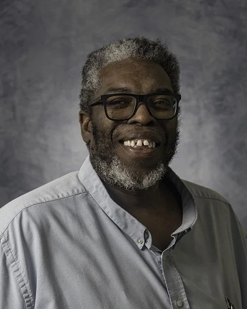 Smiling man wearing glasses and a red plaid shirt posing against a neutral background.