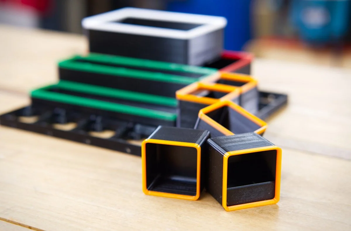 A stack of Gridfinity bins of various sizes, in the foreground there are 1x1 bins with orange rims.