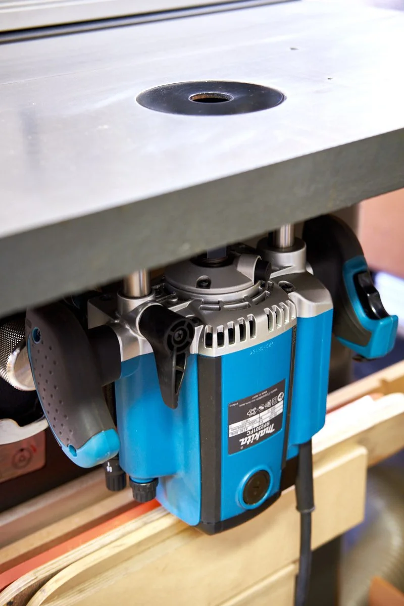 Makita RP2301FC electric router mounted upside down to a table saw router table showing the clearance insert in the cast iron top of the table saw.