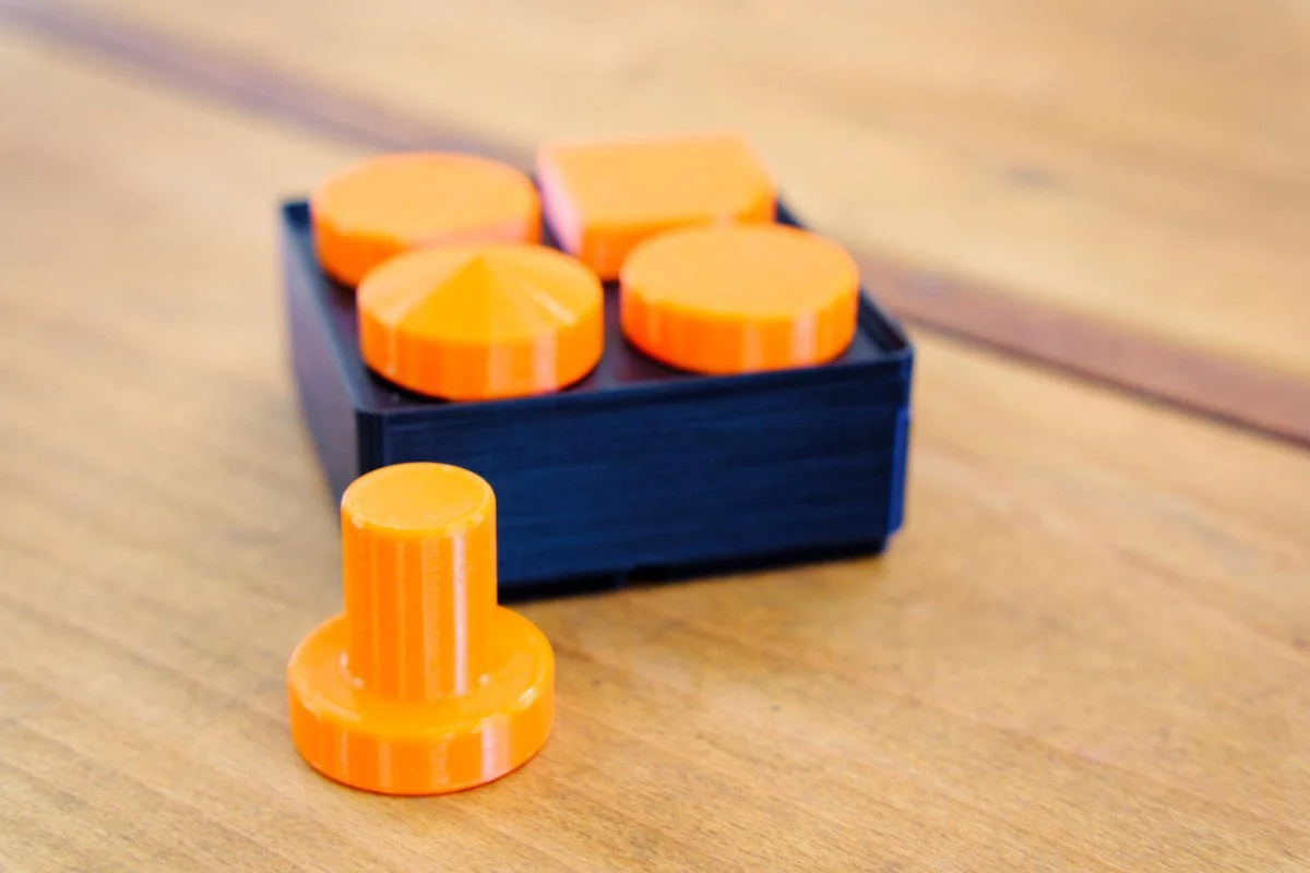 Orange, PETG 3D printed work holding dogs arranged in a dedicated Gridfinity based bin.
