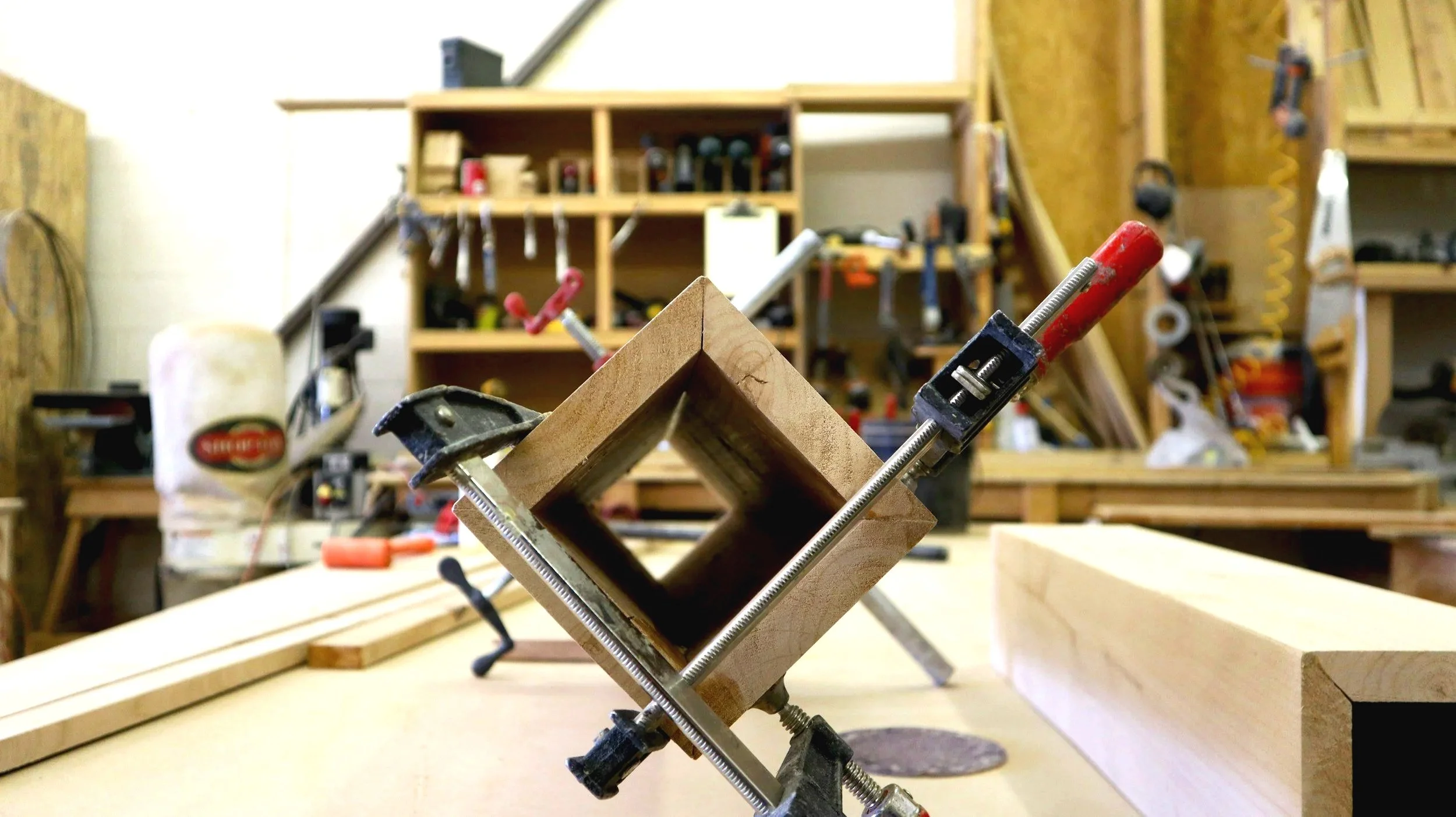 A wooden box with mitred corners being glued up and clamped with F-Clamps showing gaps between the joints.