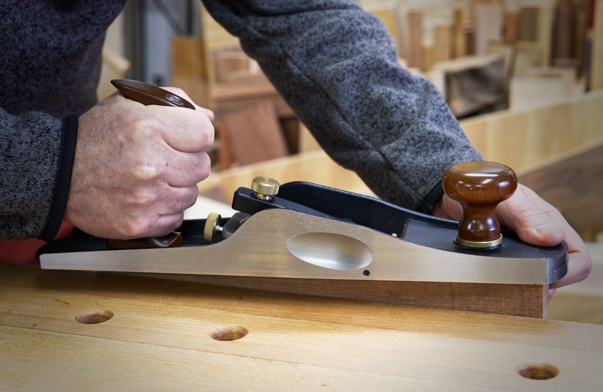 The hands of a wood worker holding the Veritas Low Angle Jack hand plane while planing wood.