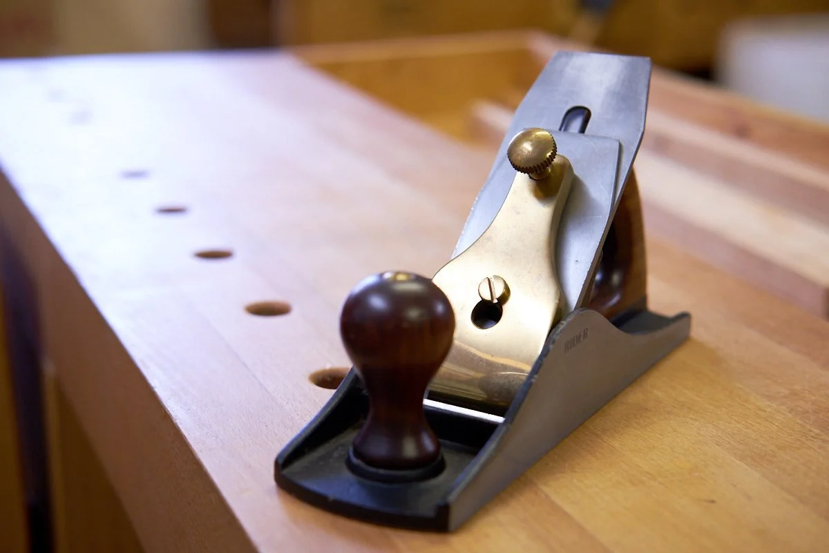 RIDER #4½ hand plane on top of a woodworking bench top in front of a row of dog holes.