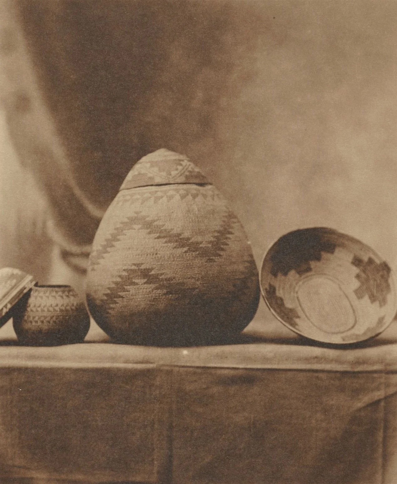 Sepia-toned photograph of four traditional woven baskets with geometric patterns, arranged on a wooden surface.
