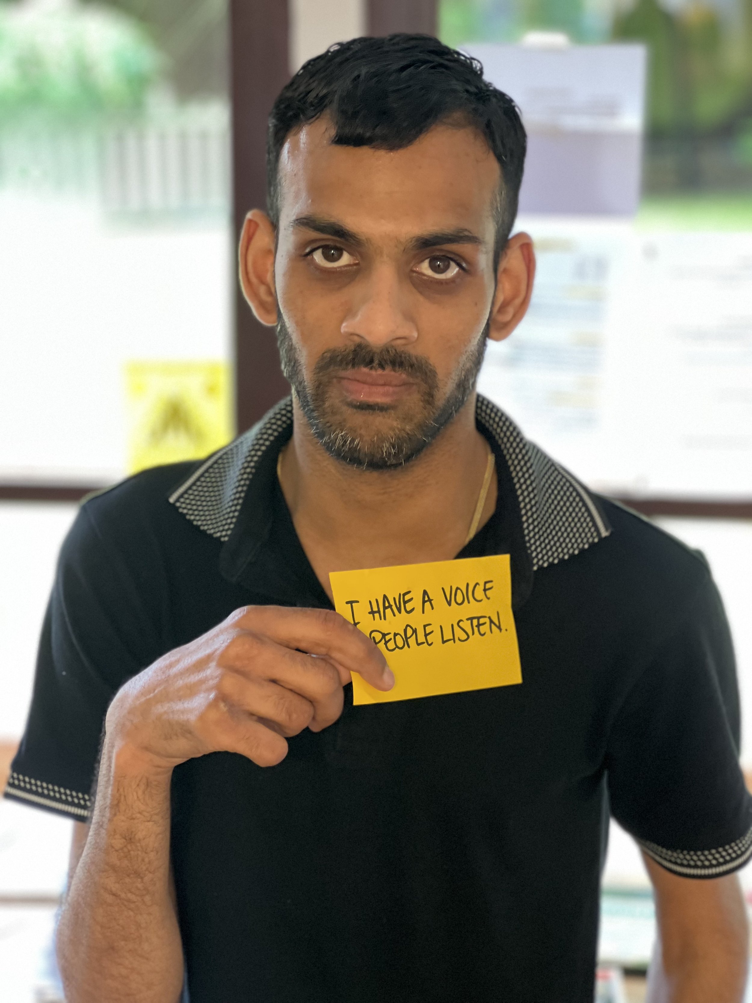 Prash is looking at the camera. He is holding a sign that says "I have a voice. People listen."