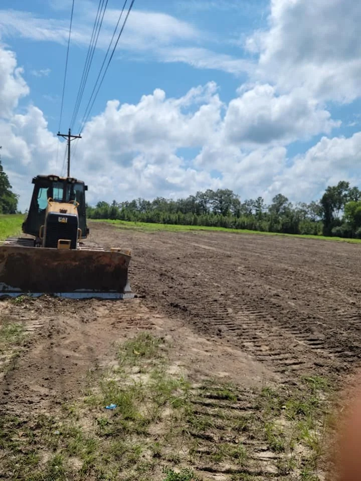A construction site with a bulldozer working on a dirt lot under a partly cloudy sky.