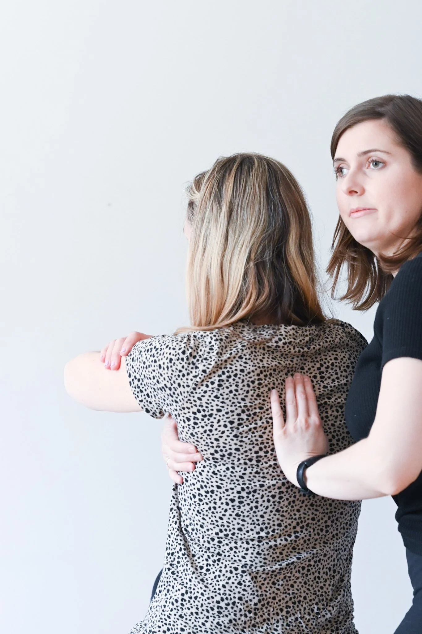 A person assisting another person with a physical therapy or chiropractic adjustment, focusing on the back and shoulders.