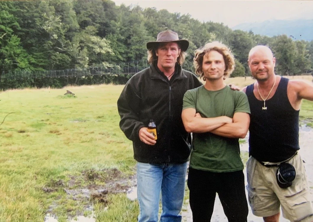 Three men posing in front of the Routeburn Trail Head in New Zealand
