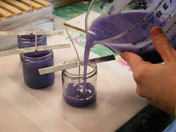 Purple liquid being poured into a small glass jar from a measuring cup, with two other jars of the same liquid nearby, all on a work surface.