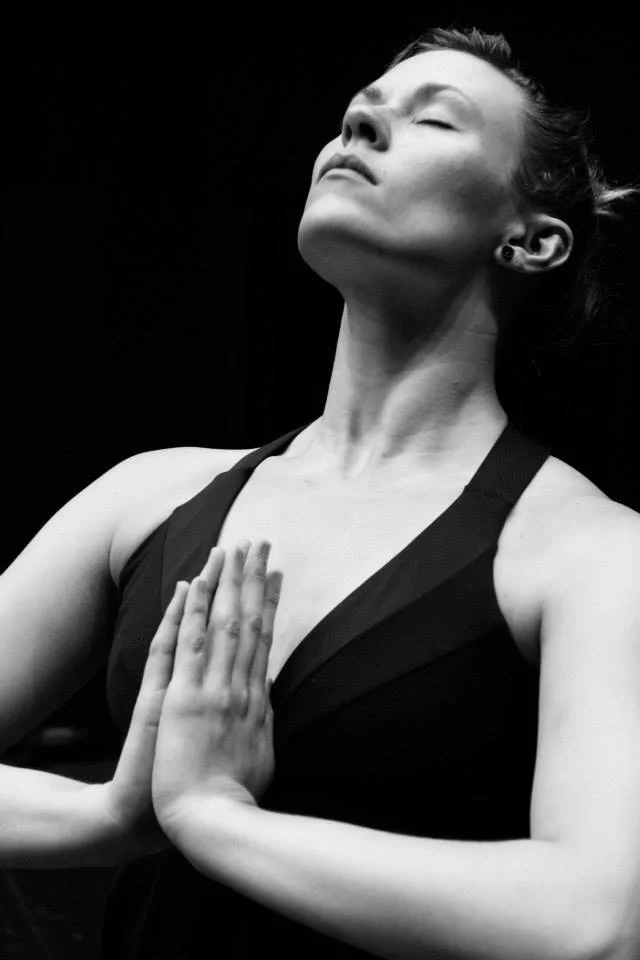 A woman practicing yoga or meditation with eyes closed and hands pressed together in front of her chest.