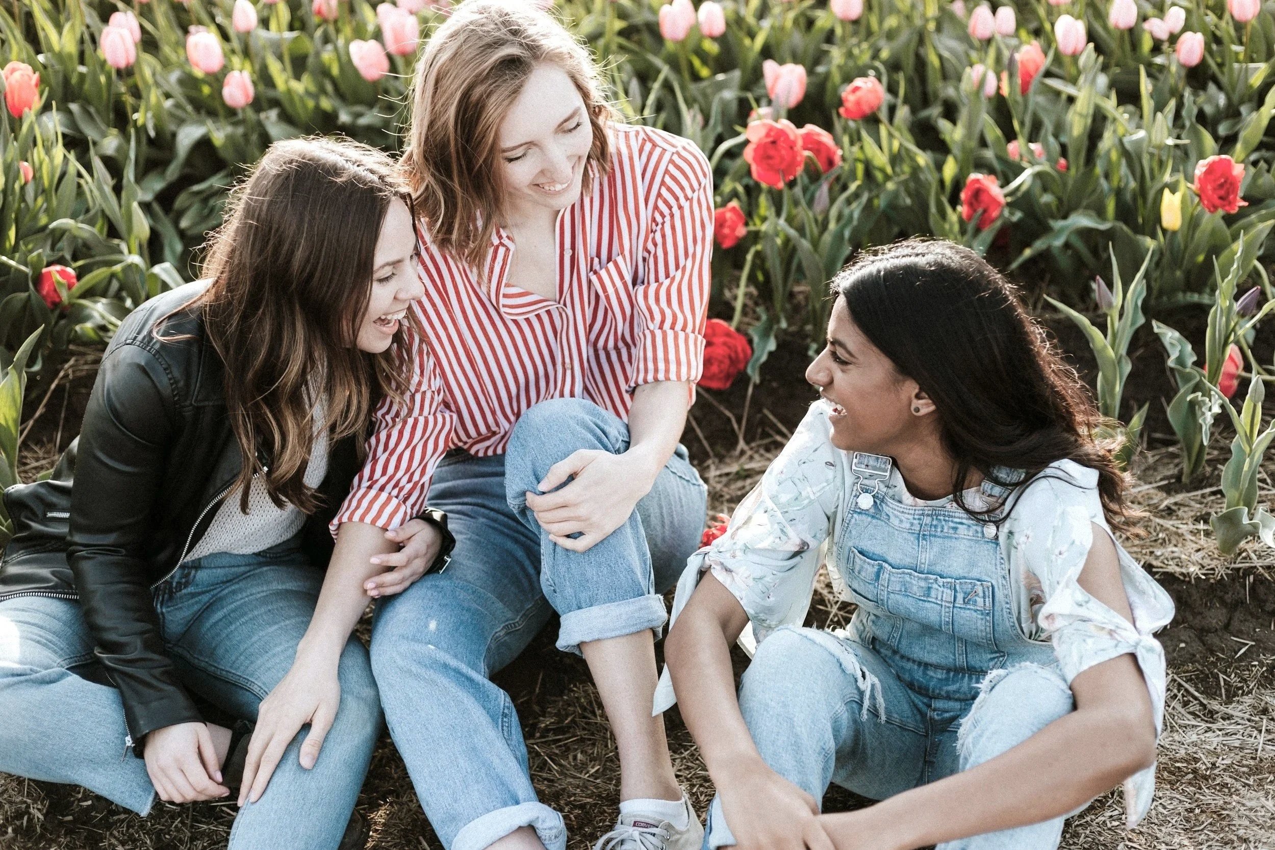 Three women sitting on the ground among tulips, laughing and talking.