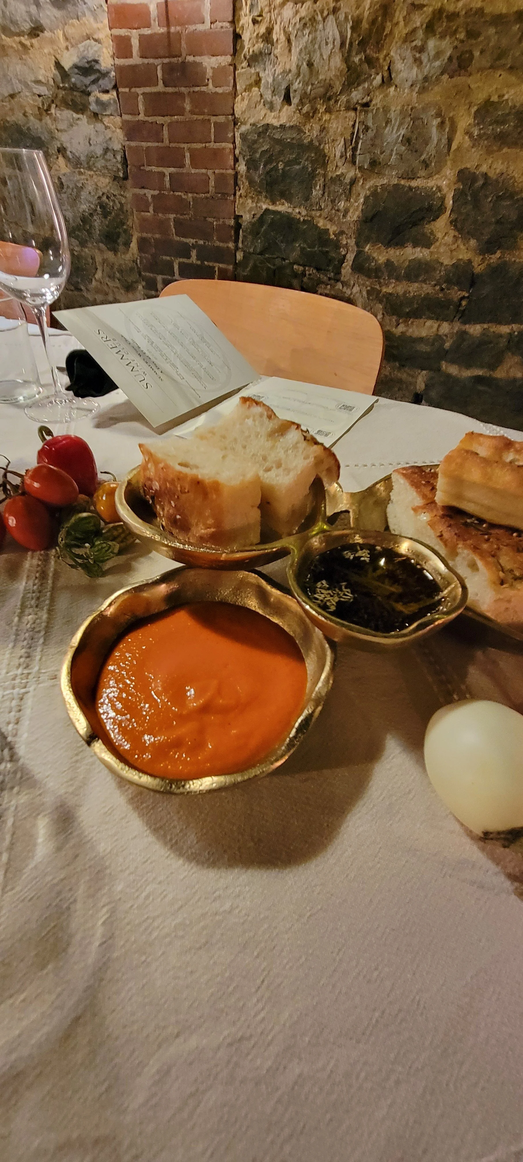 A dining table with various dishes including bread, tomato, and sauces, set against a brick and stone wall.