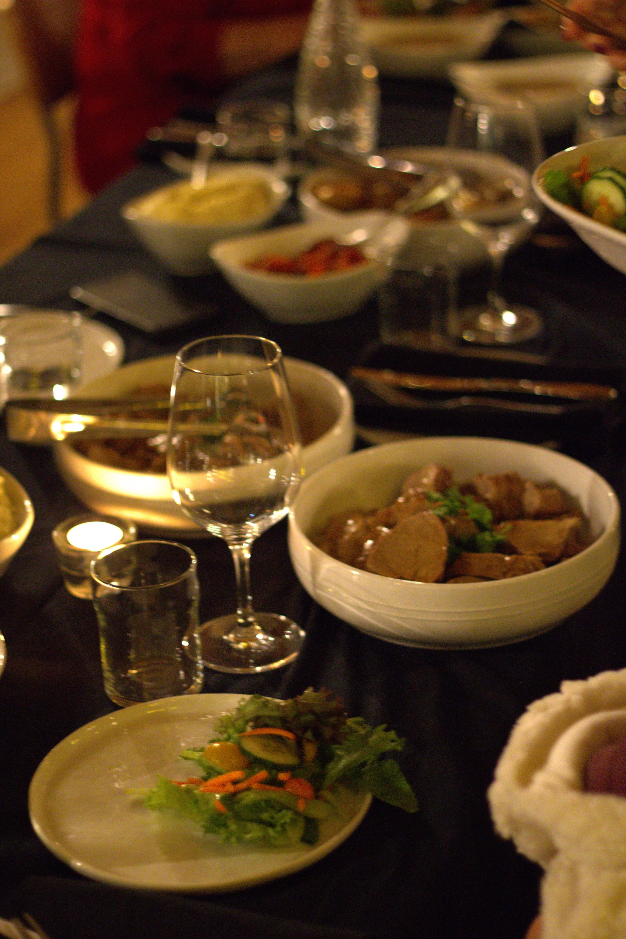 A table set for a meal with various dishes, including bowls of salad, meat, and side dishes, along with wine glasses, water glasses, and candles.