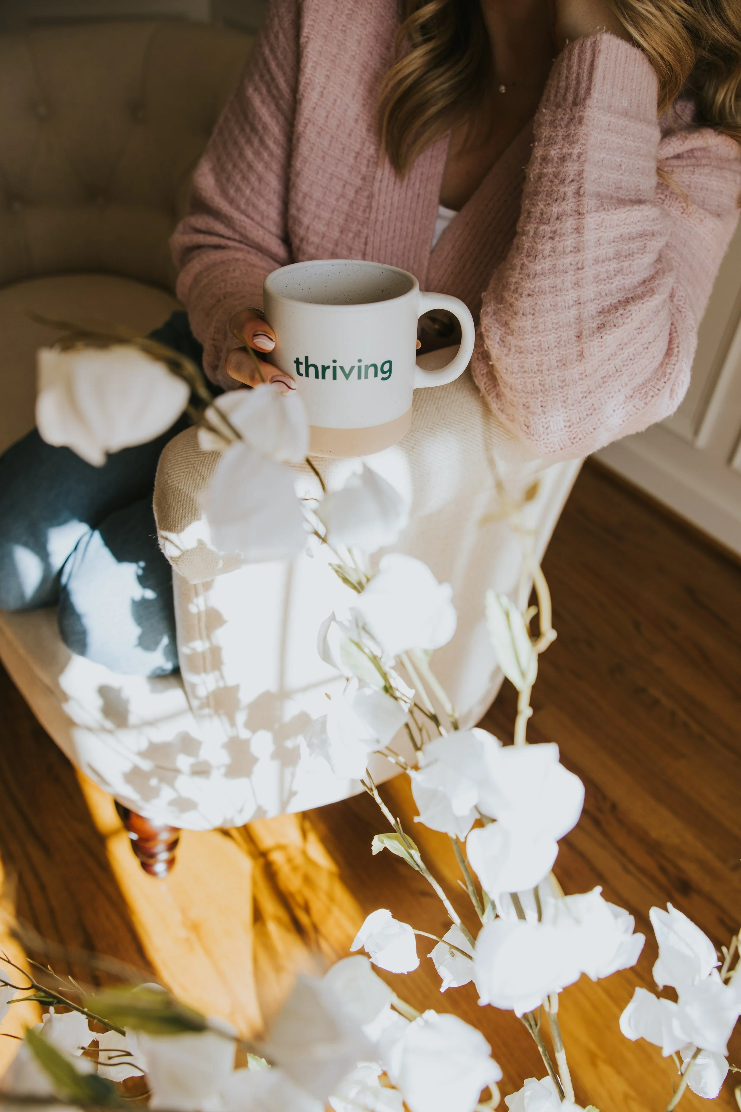 Woman holding a mug that says thriving surrounded by white flowers