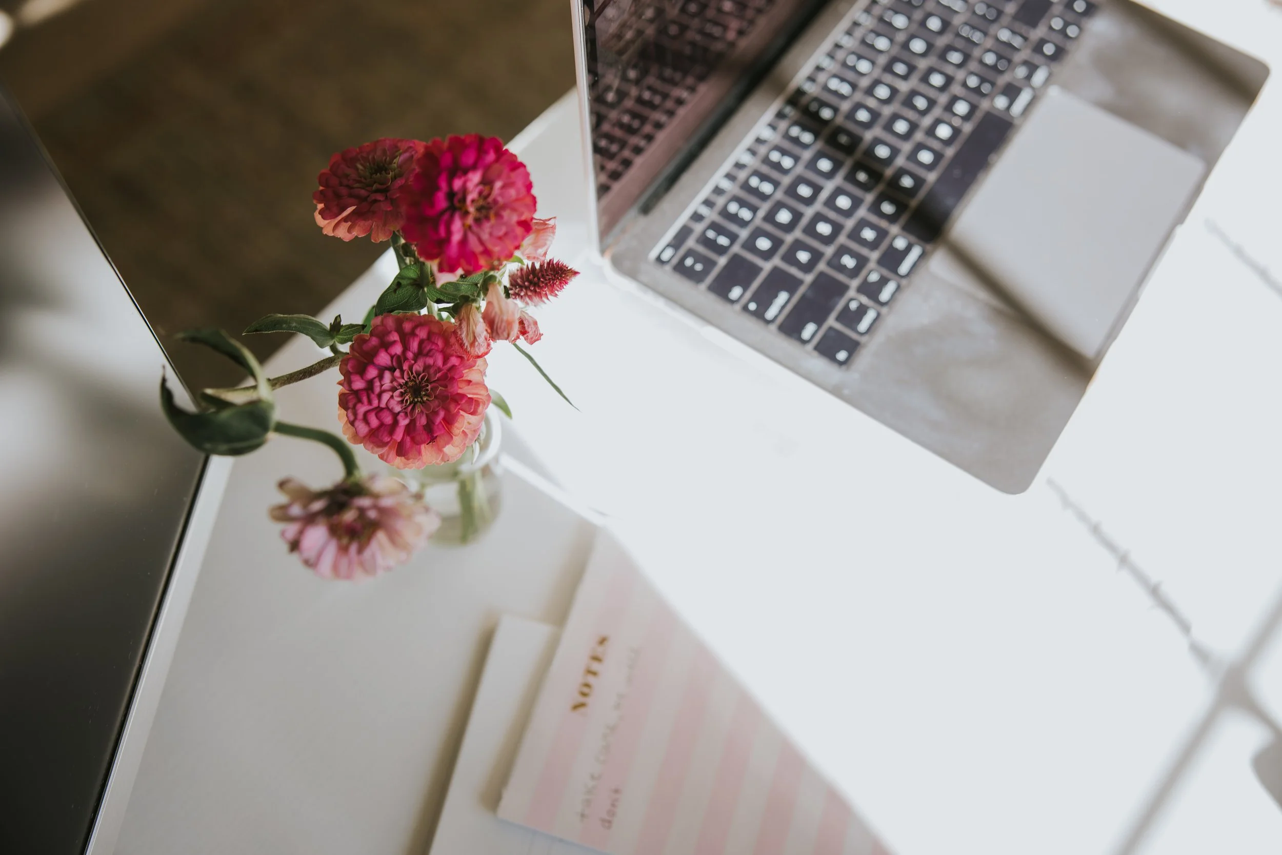Pink flowers styled next to a laptop and notepad