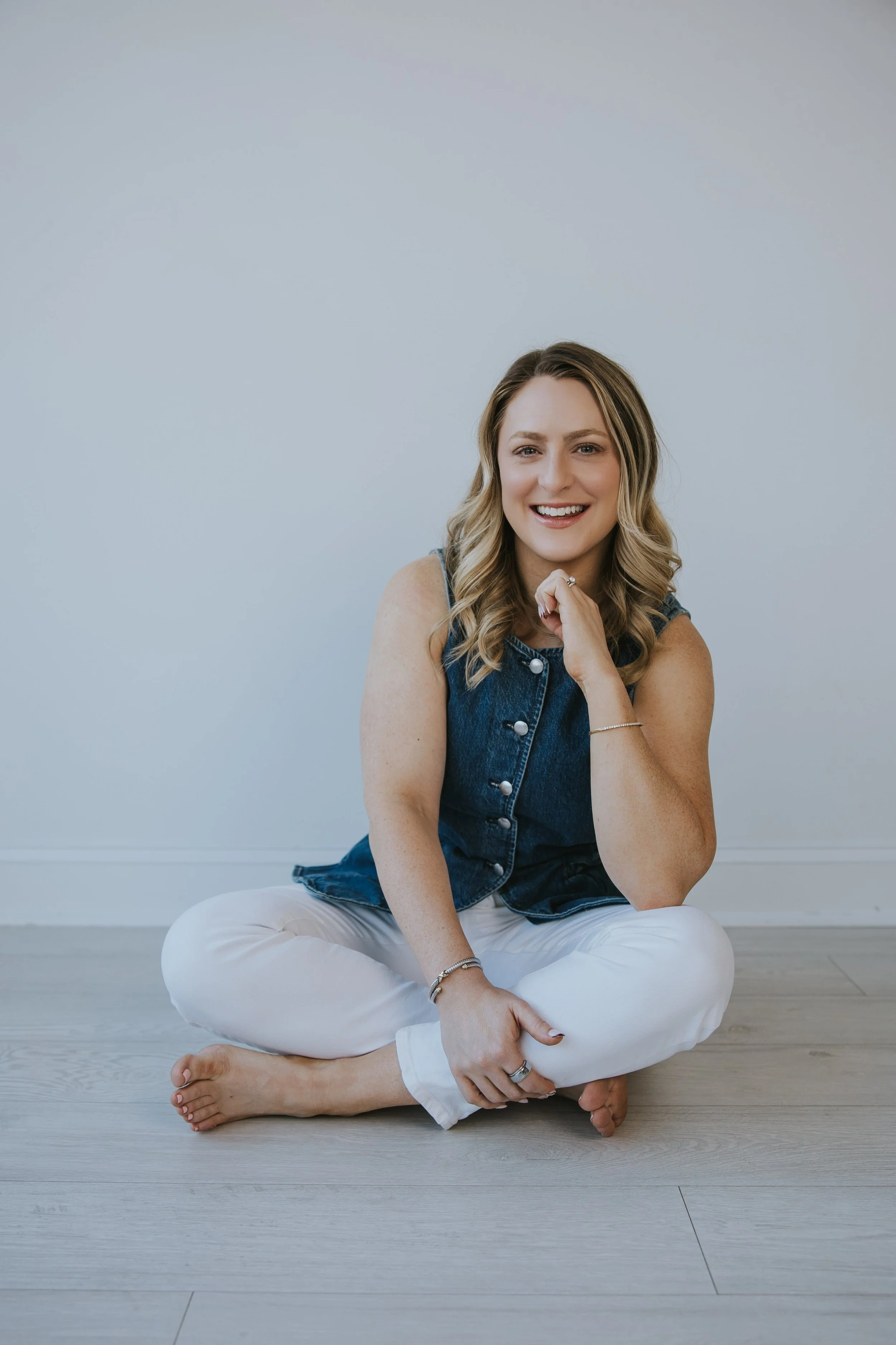 kylie lambert smiling at camera sitting criss cross on the floor in white jeans and jean vest