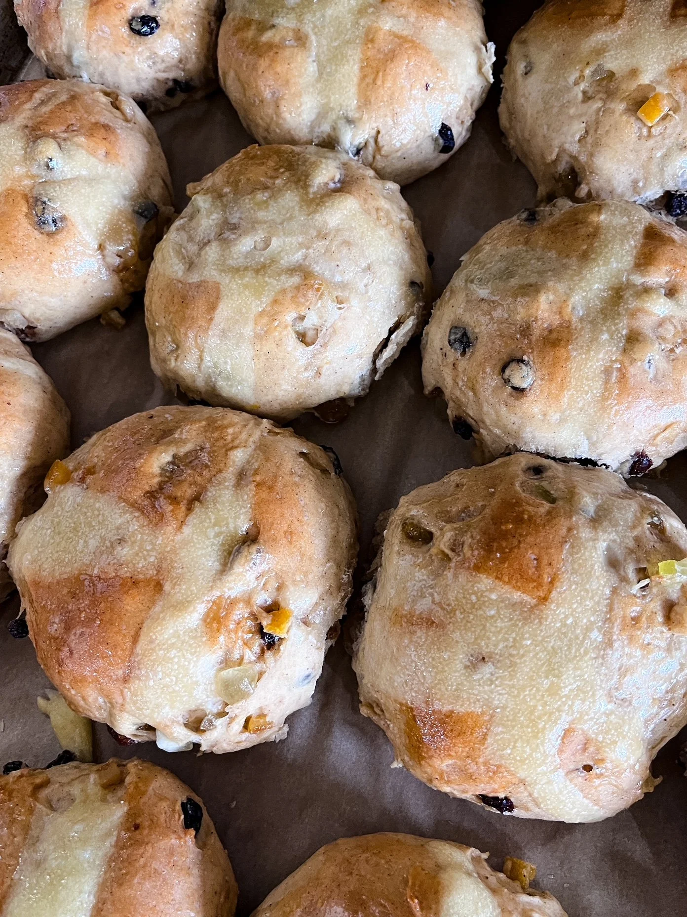 Baked hot cross buns with golden brown tops and visible bits of raisins and nuts.