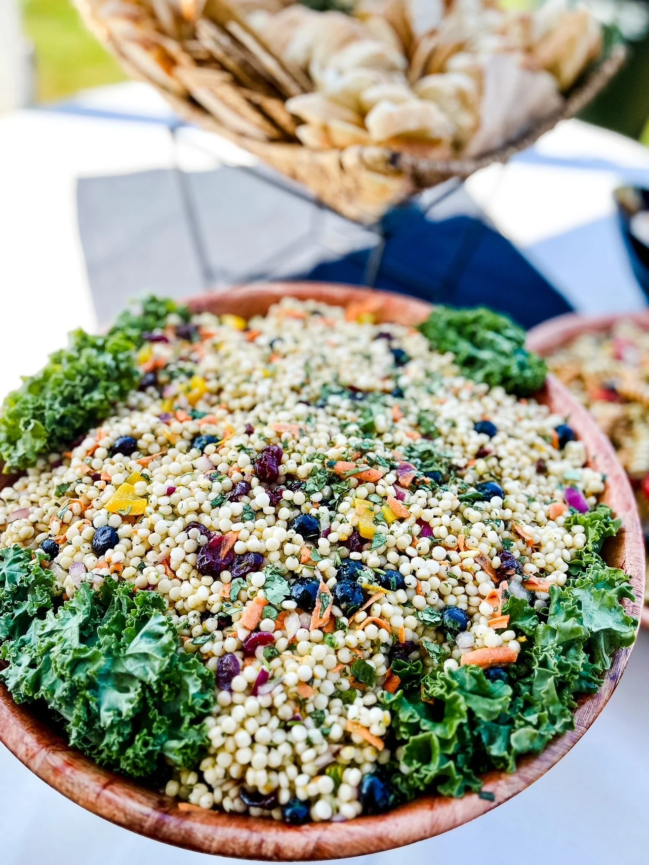 A large wooden bowl filled with a colorful cous cous salad.