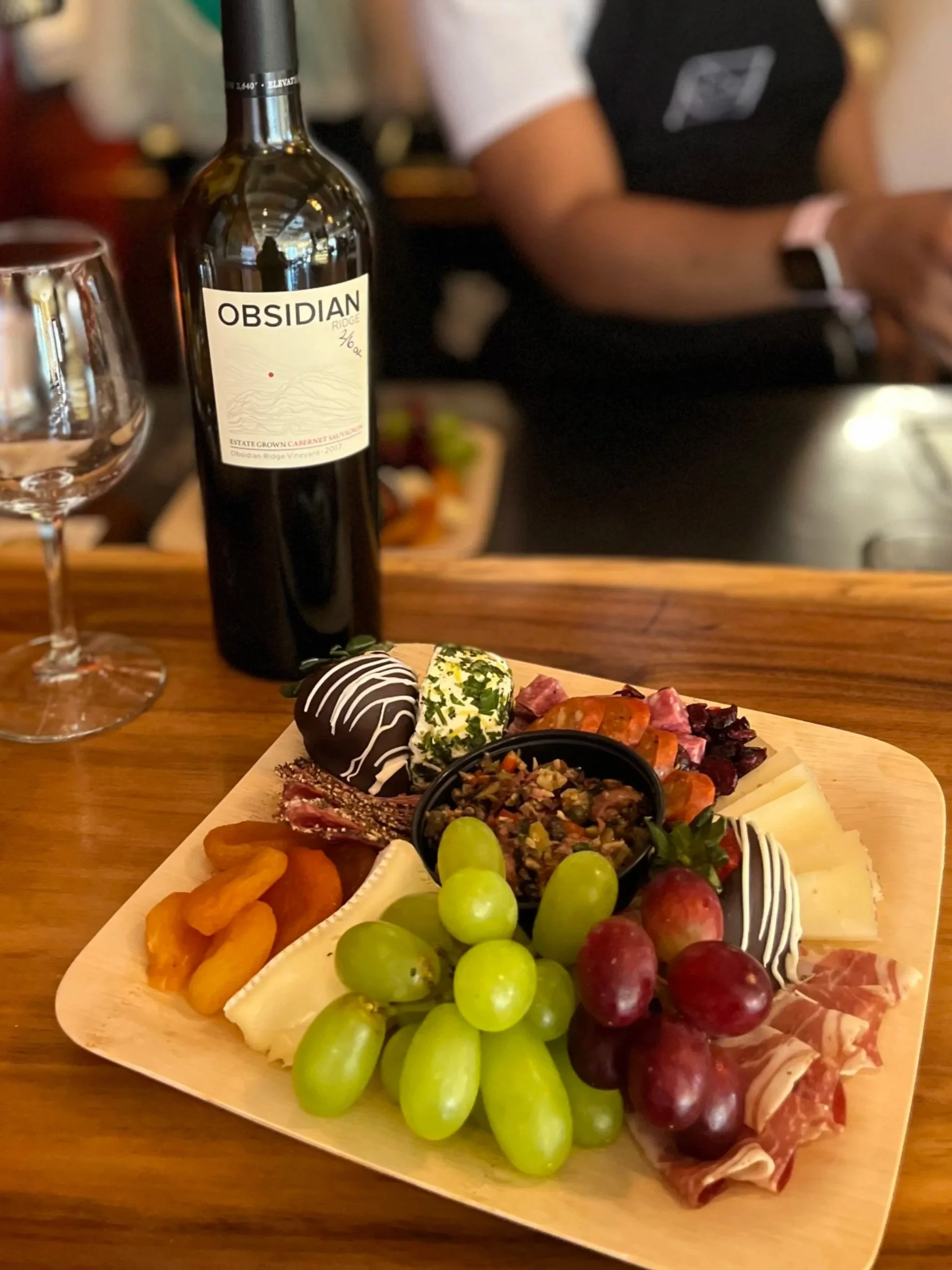 Barista working behind counter with grazing board and wine on counter