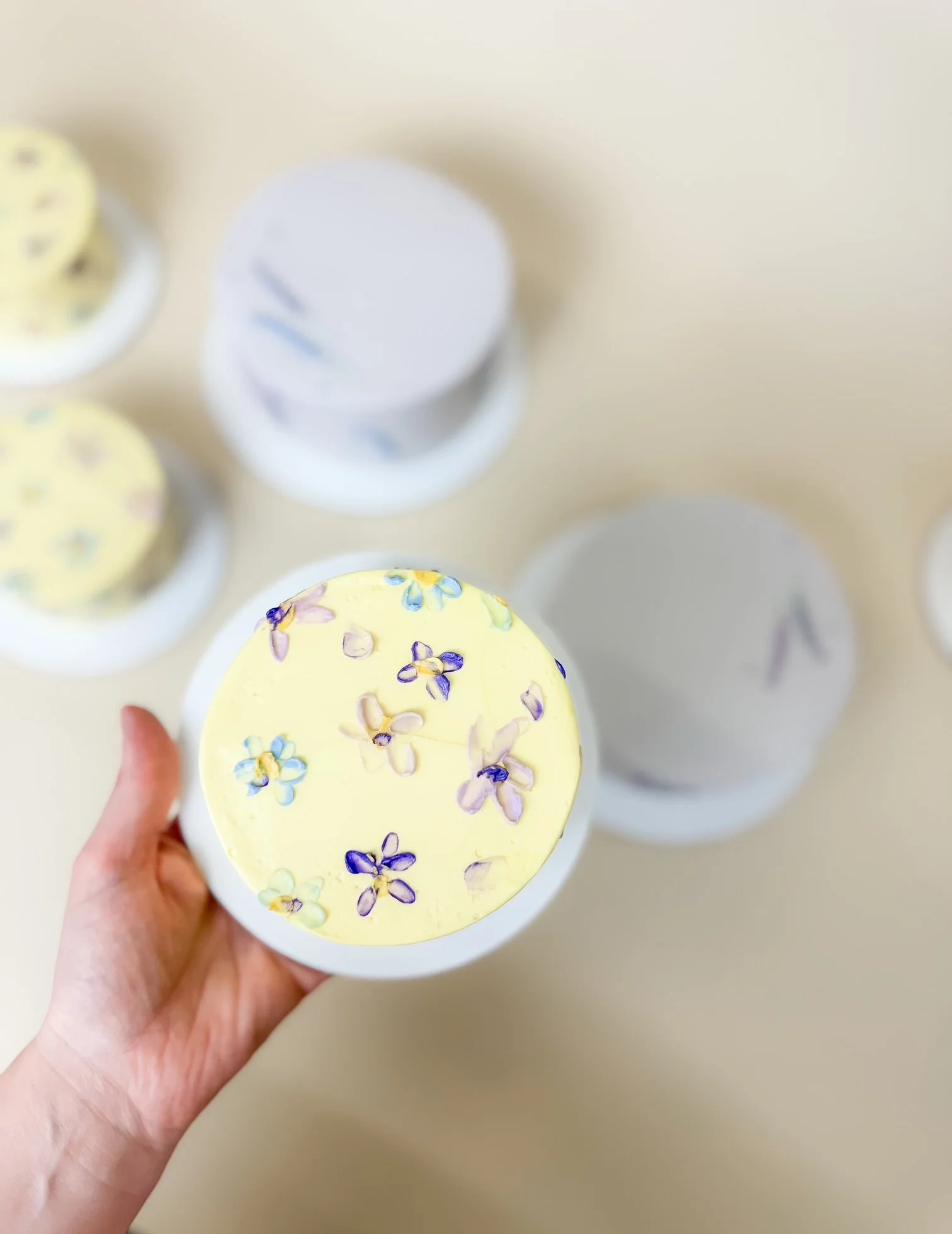 A hand holding a small yellow frosted cake with buttercream flowers