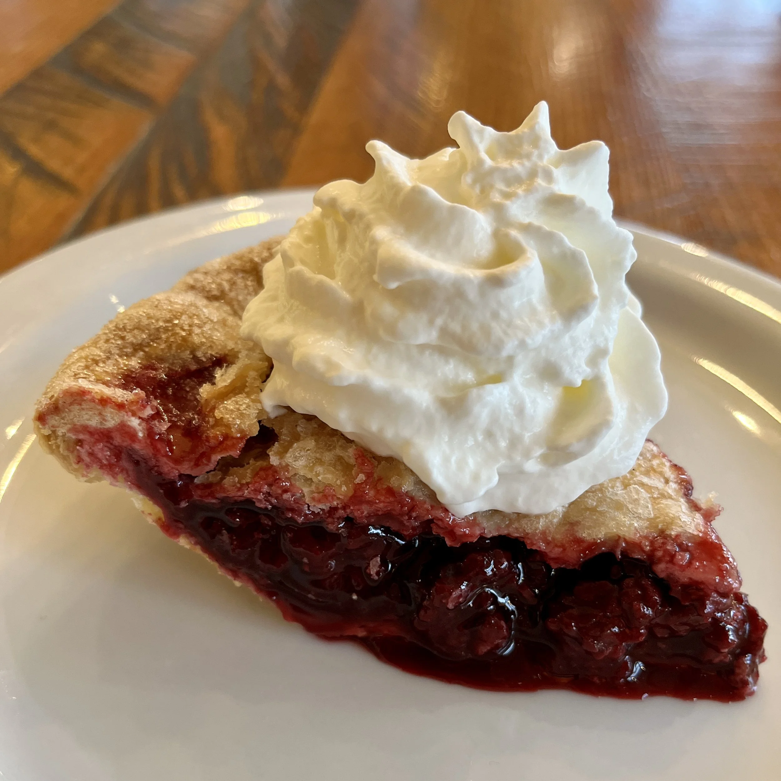 Slice of cherry pie topped with whipped cream on white plate