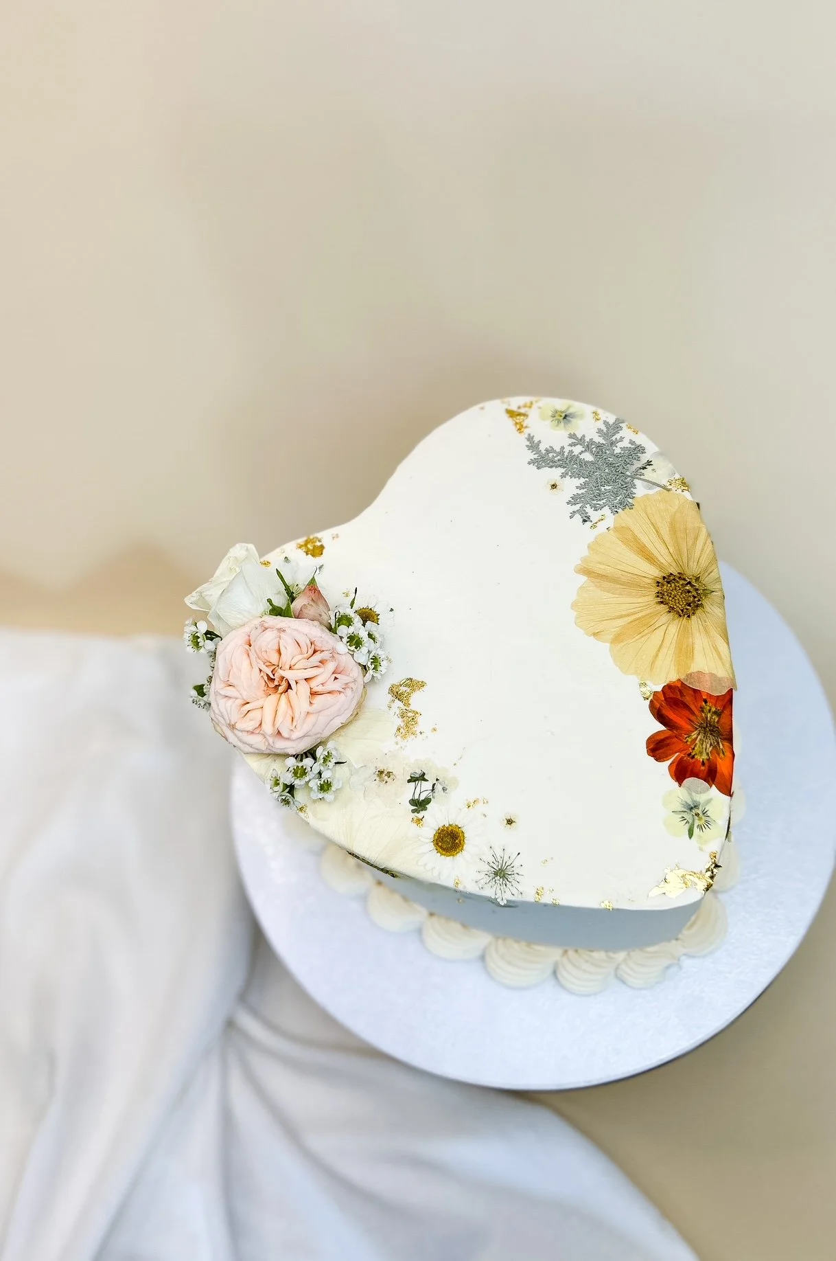 Heart-shaped wedding cake decorated with pressed flowers and edible gold accents