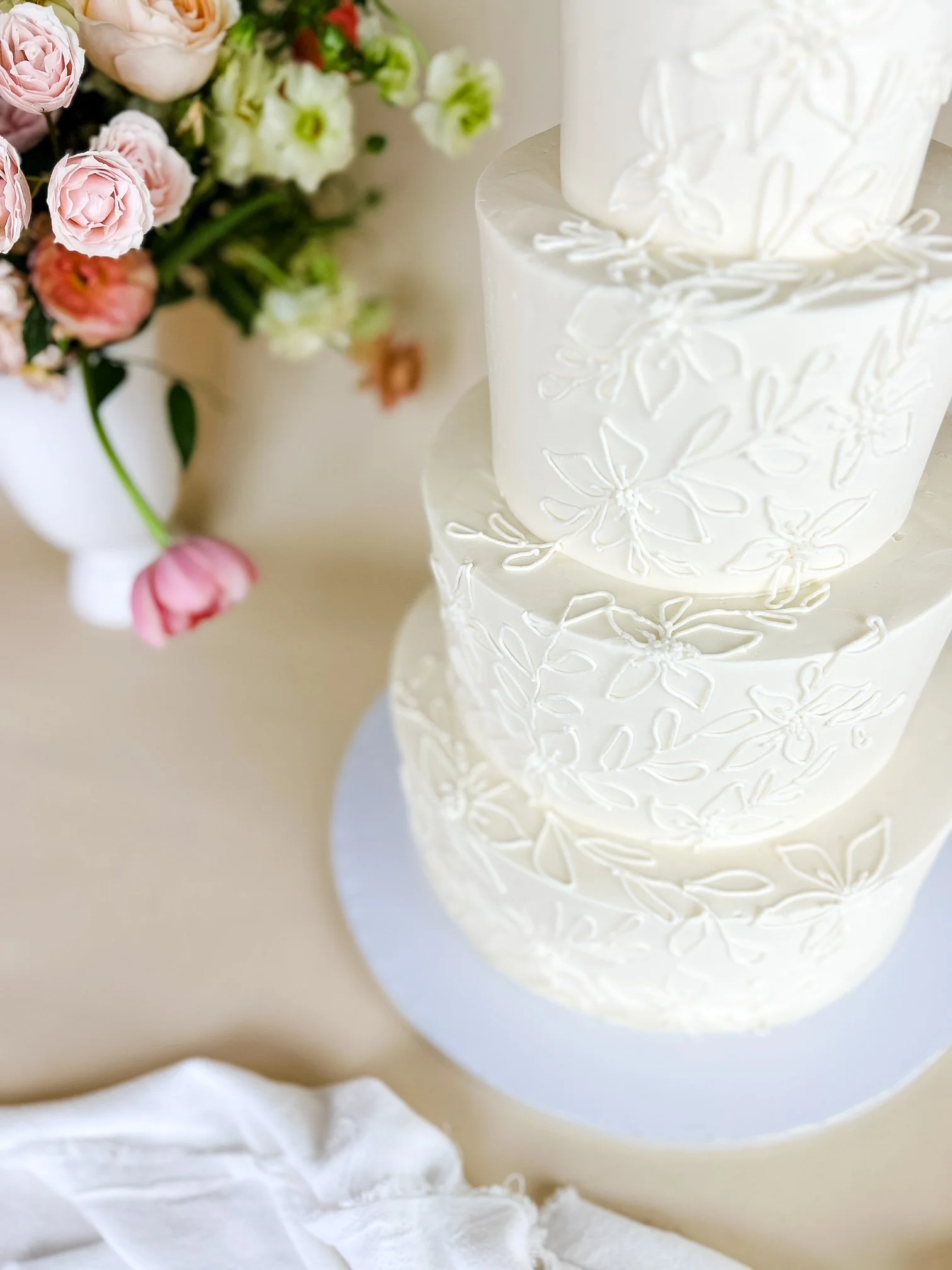 A tall, multi-tiered white wedding cake with delicate floral piping design