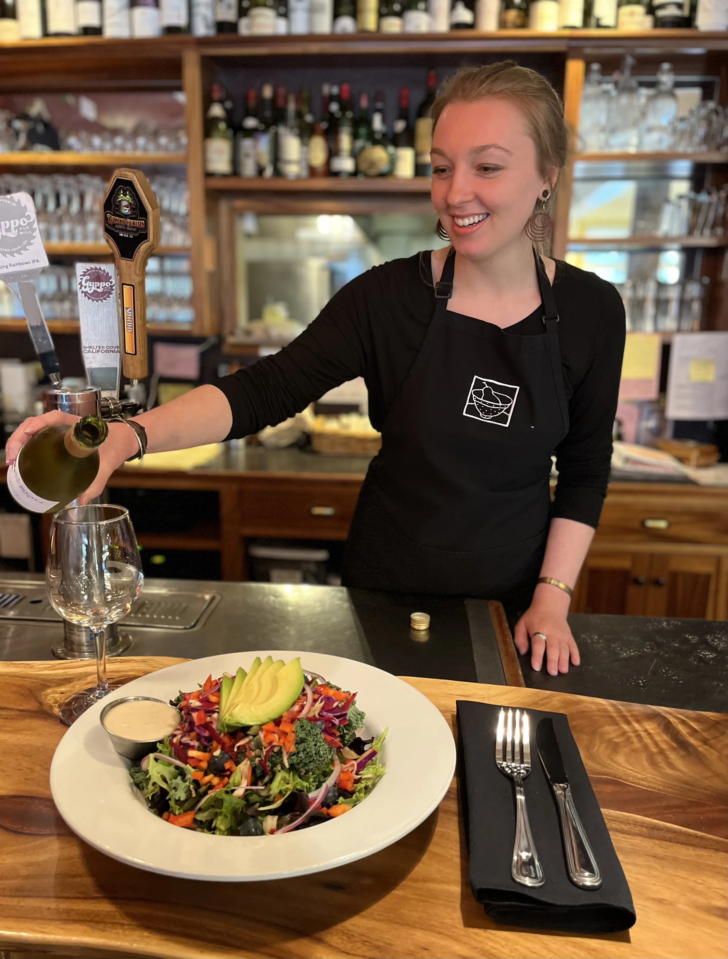 Wait person pouring white wine near bowl of "buddha bowl" salad