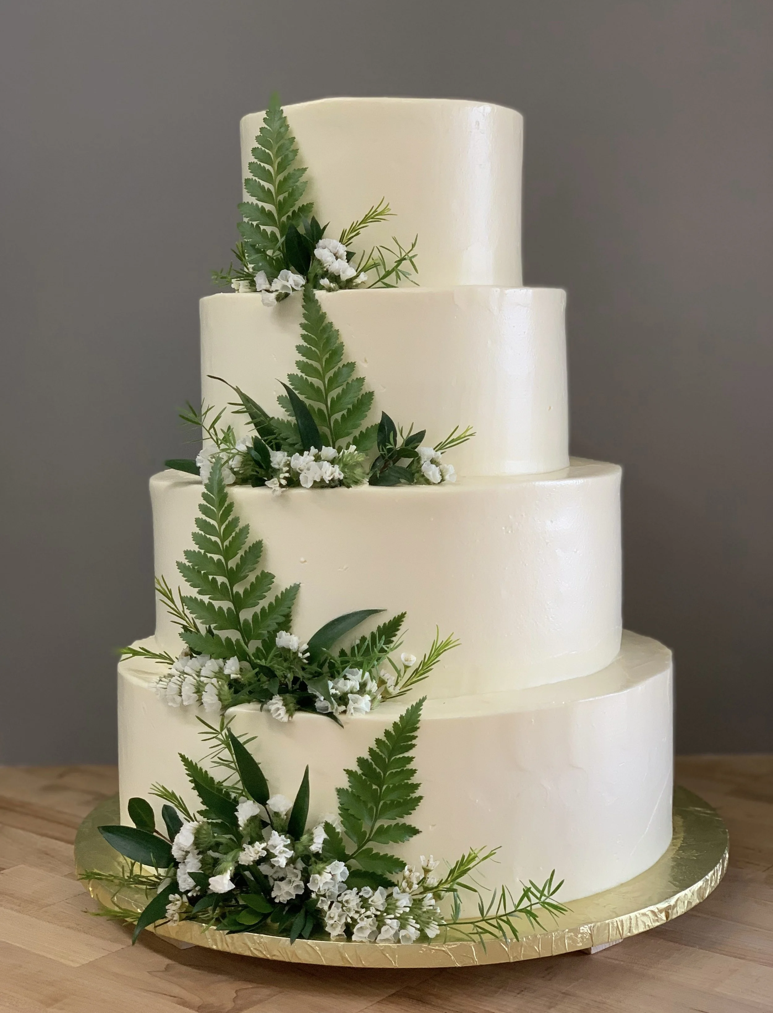 Four-tiered white wedding cake decorated with ferns