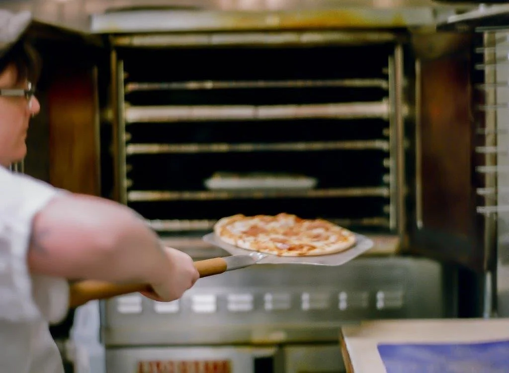 Cook putting pizza in the pizza oven