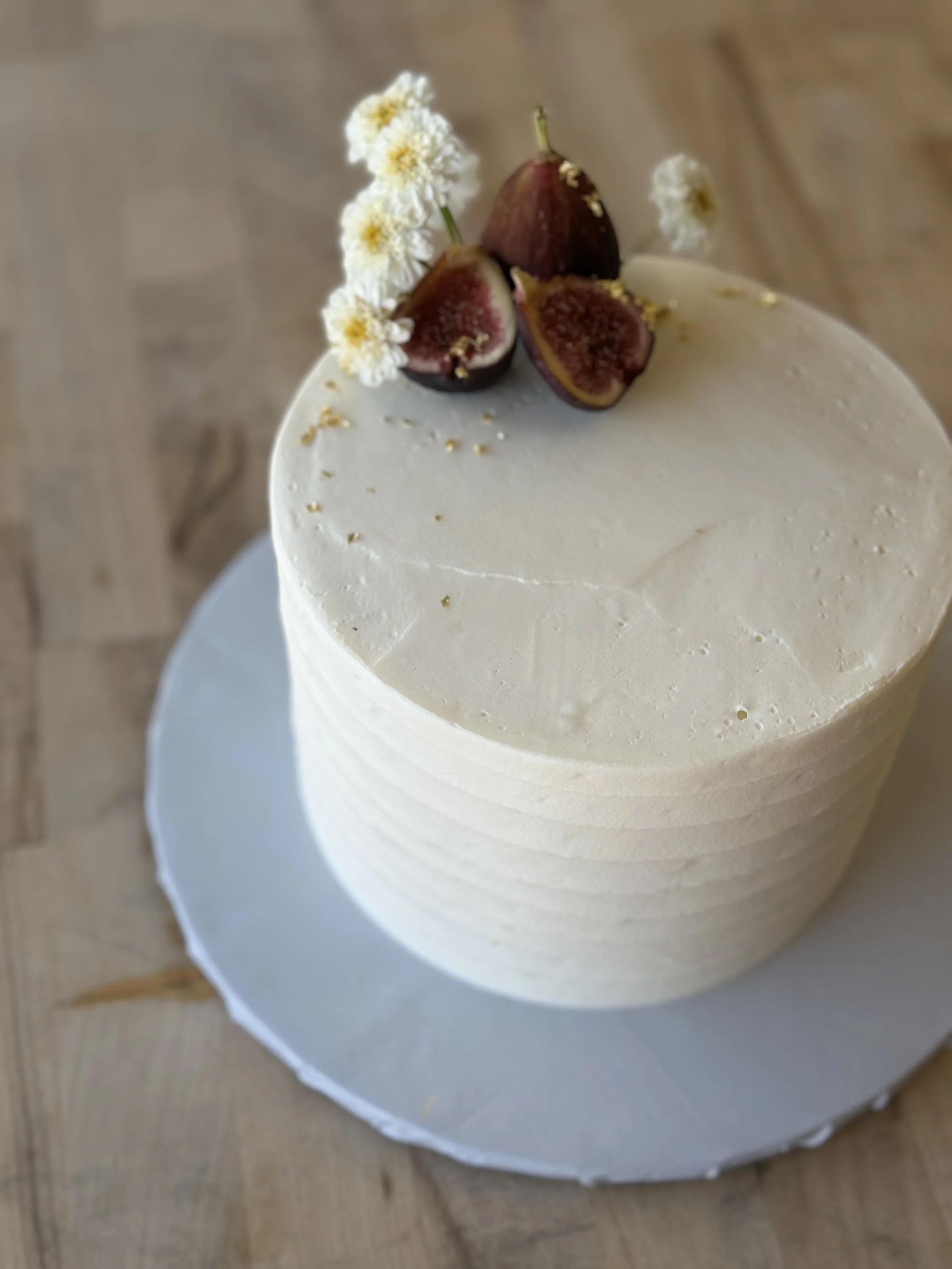 A small, white cake decorated with fresh figs and small white flowers on top