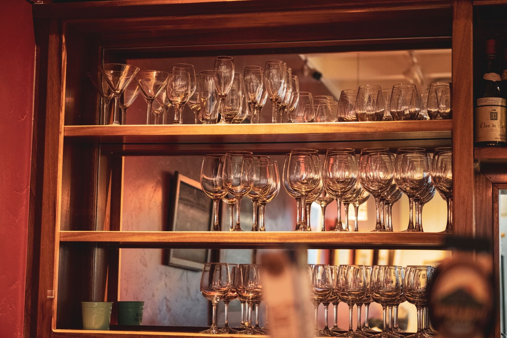 Wooden shelving unit with multiple rows of wine glasses in a warm bistro setting.