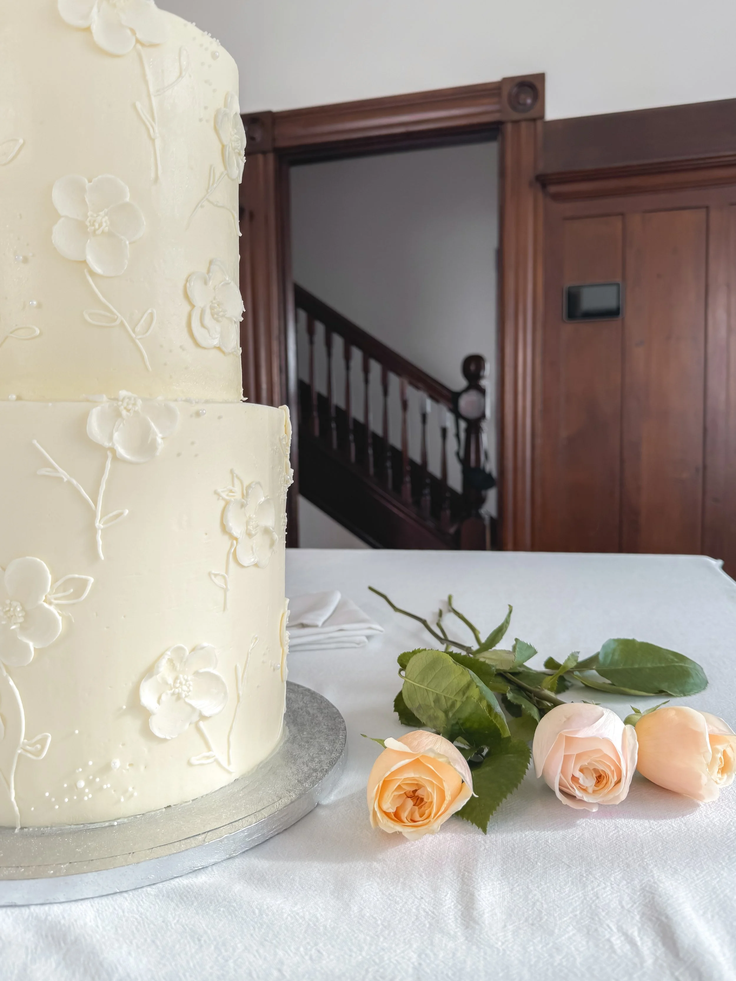 A three-tiered white wedding cake decorated with floral designs