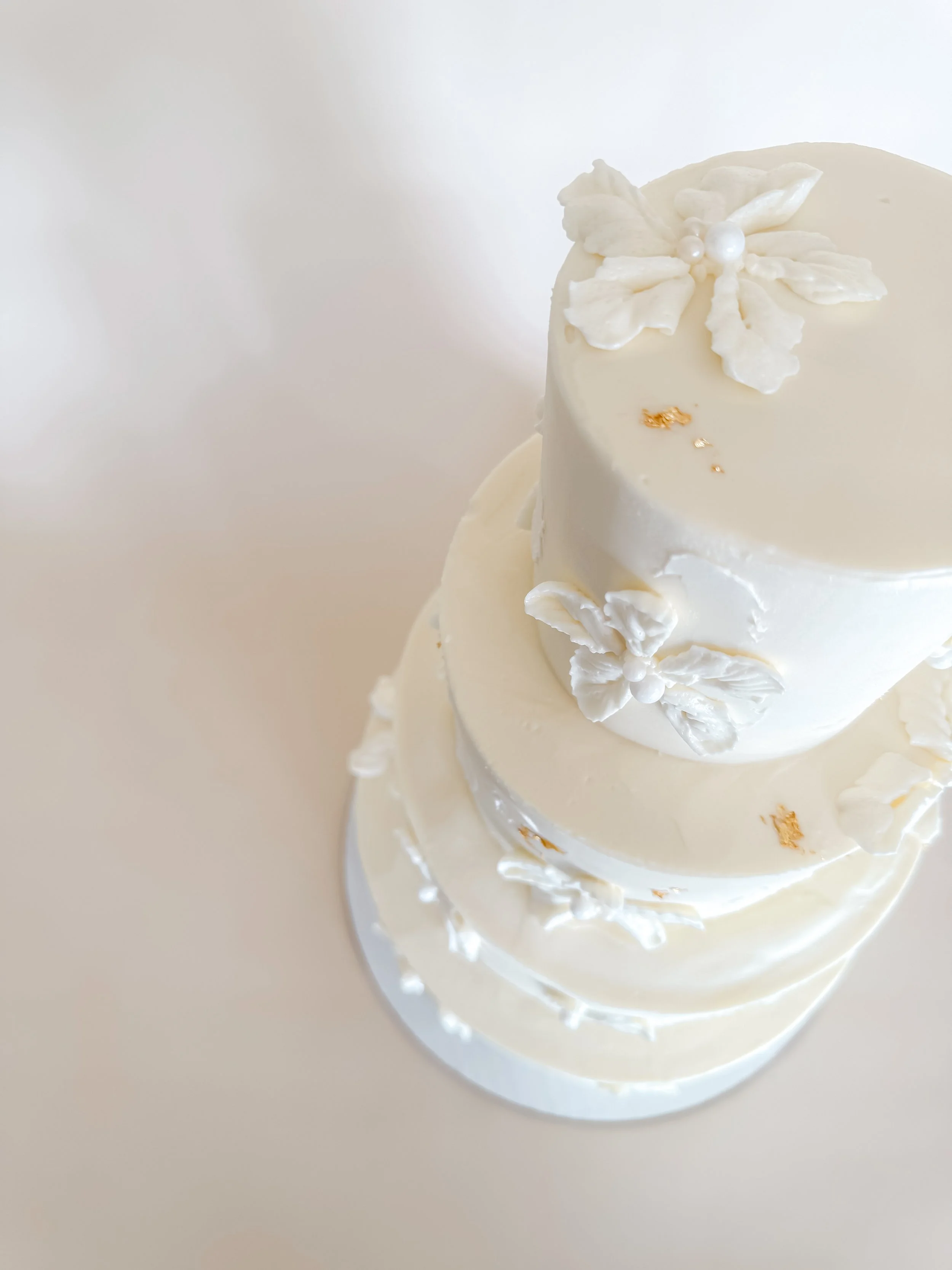 A three-tiered white cake decorated with poinsettia flowers and small pearls