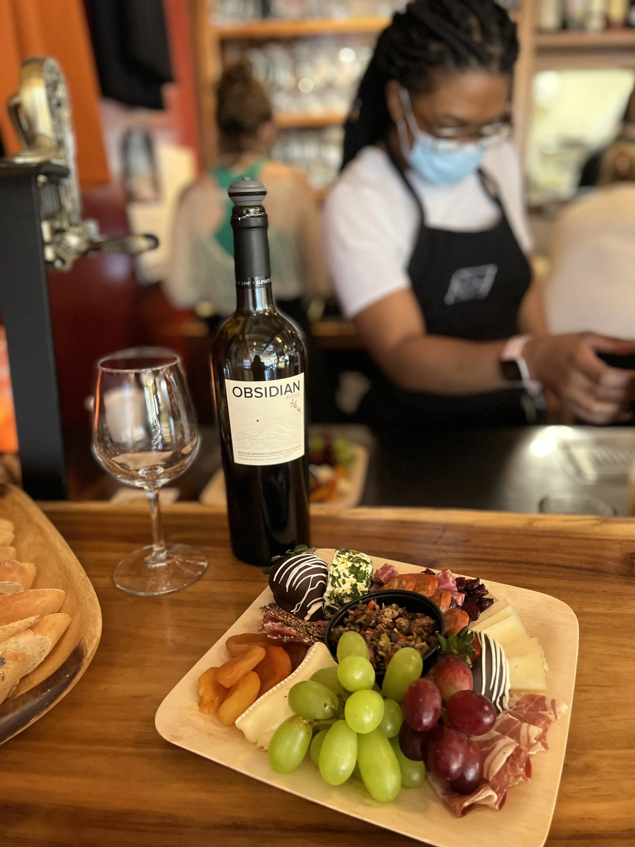 Barista working behind counter with grazing board and wine on counter