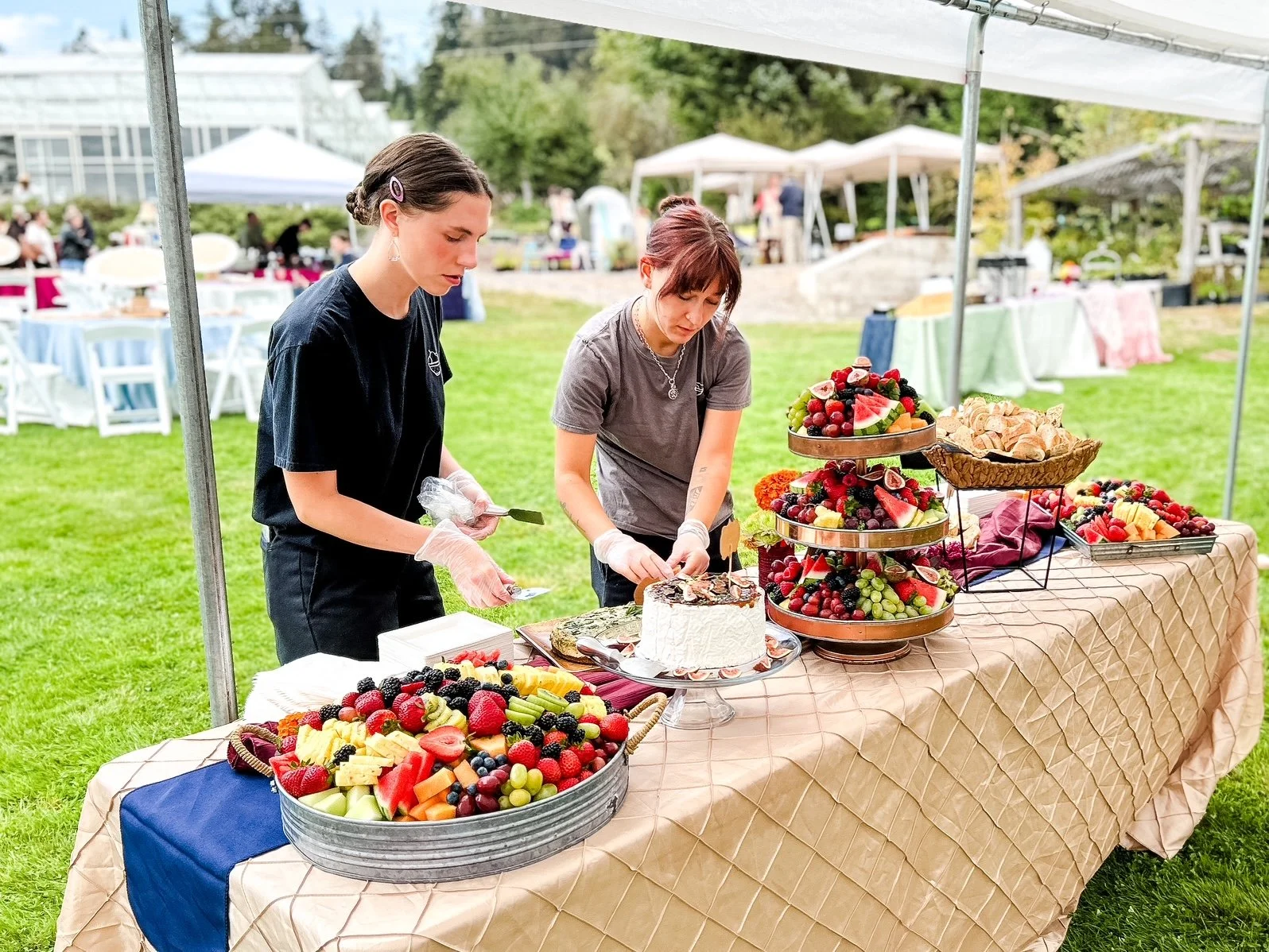 Two women arranging a fruit platter at an outdoor event