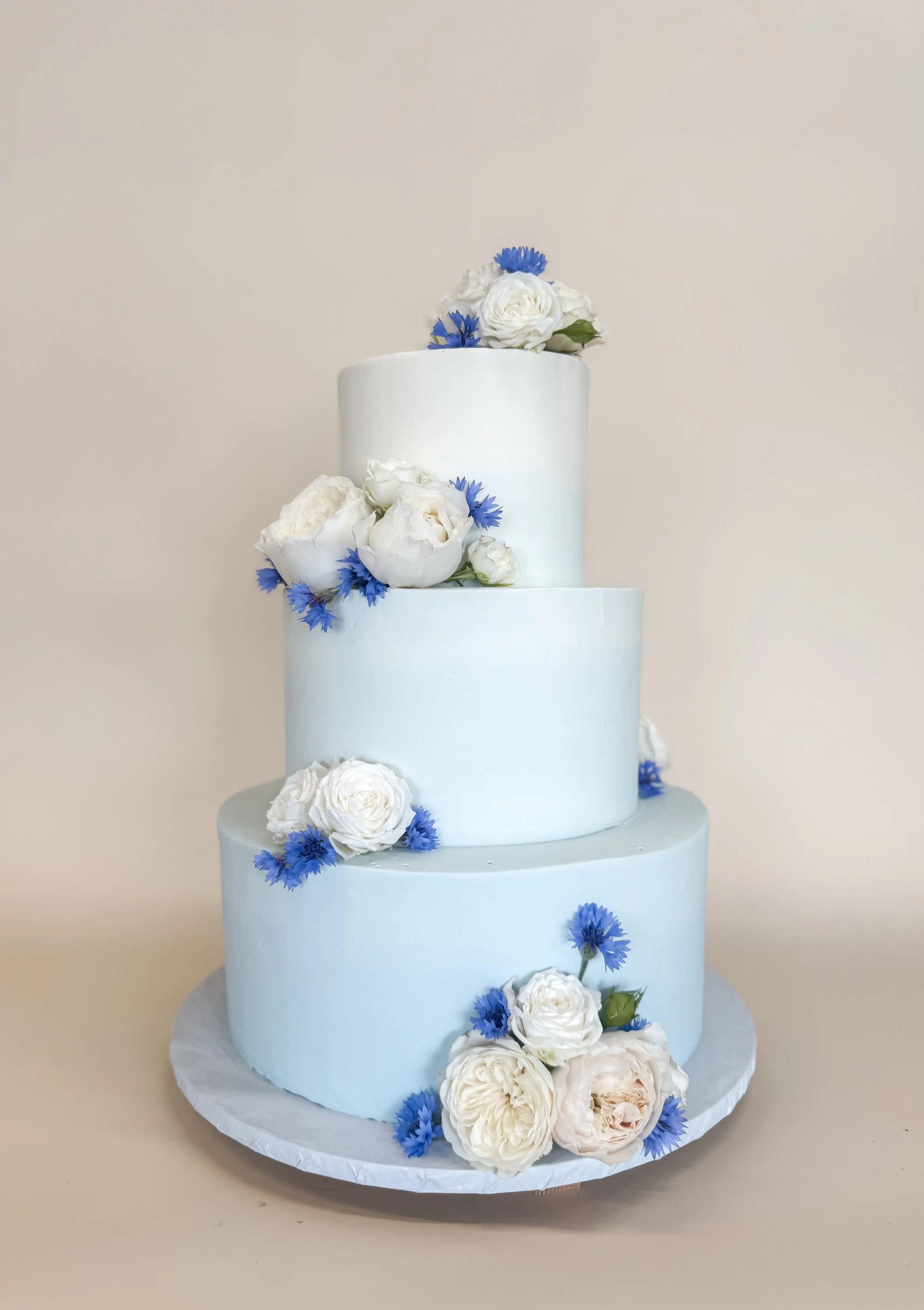 A three-tiered wedding cake frosted with a light blue ombre buttercream frosting