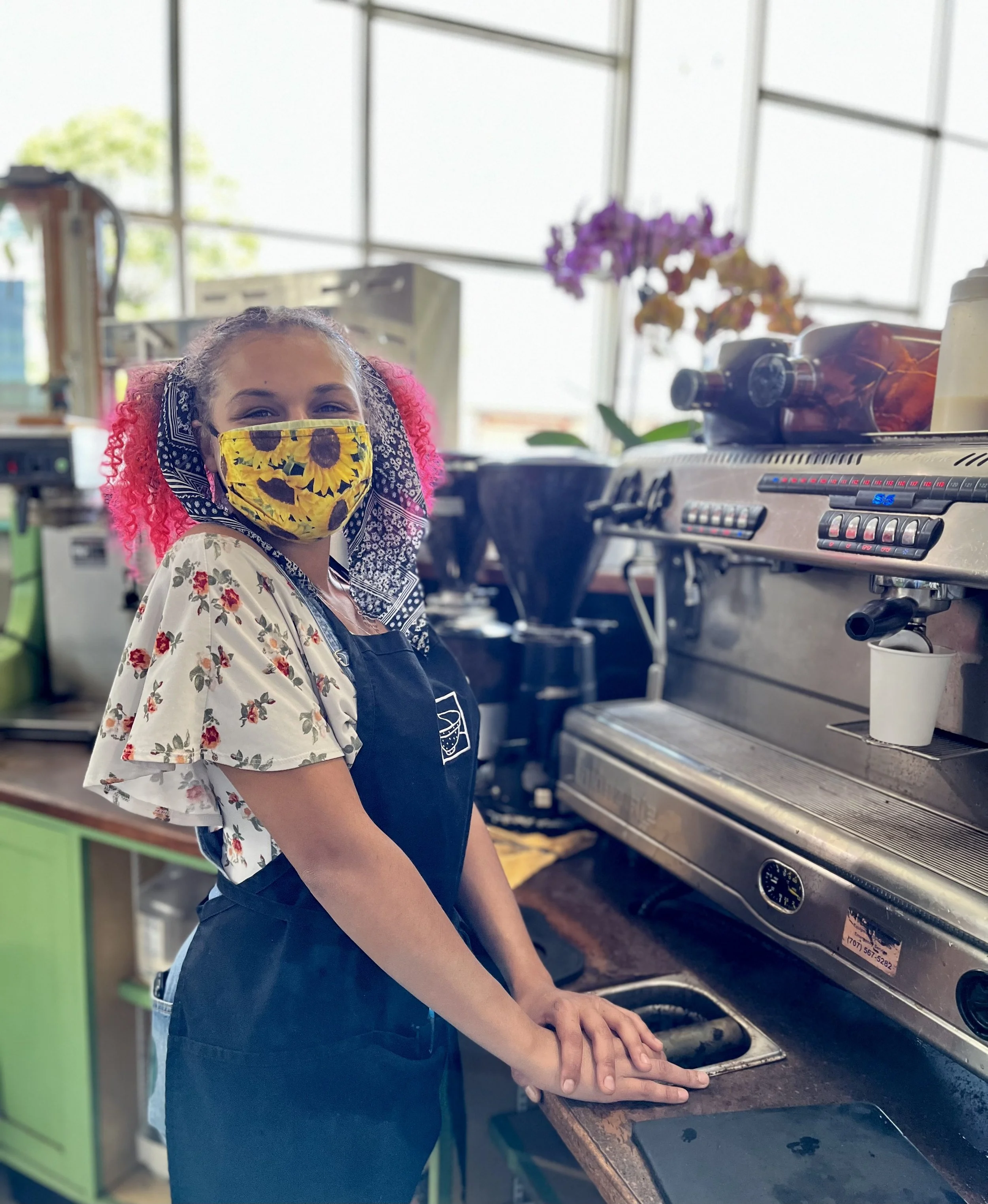 Barista wearing a sunflower patterned face mask and apron