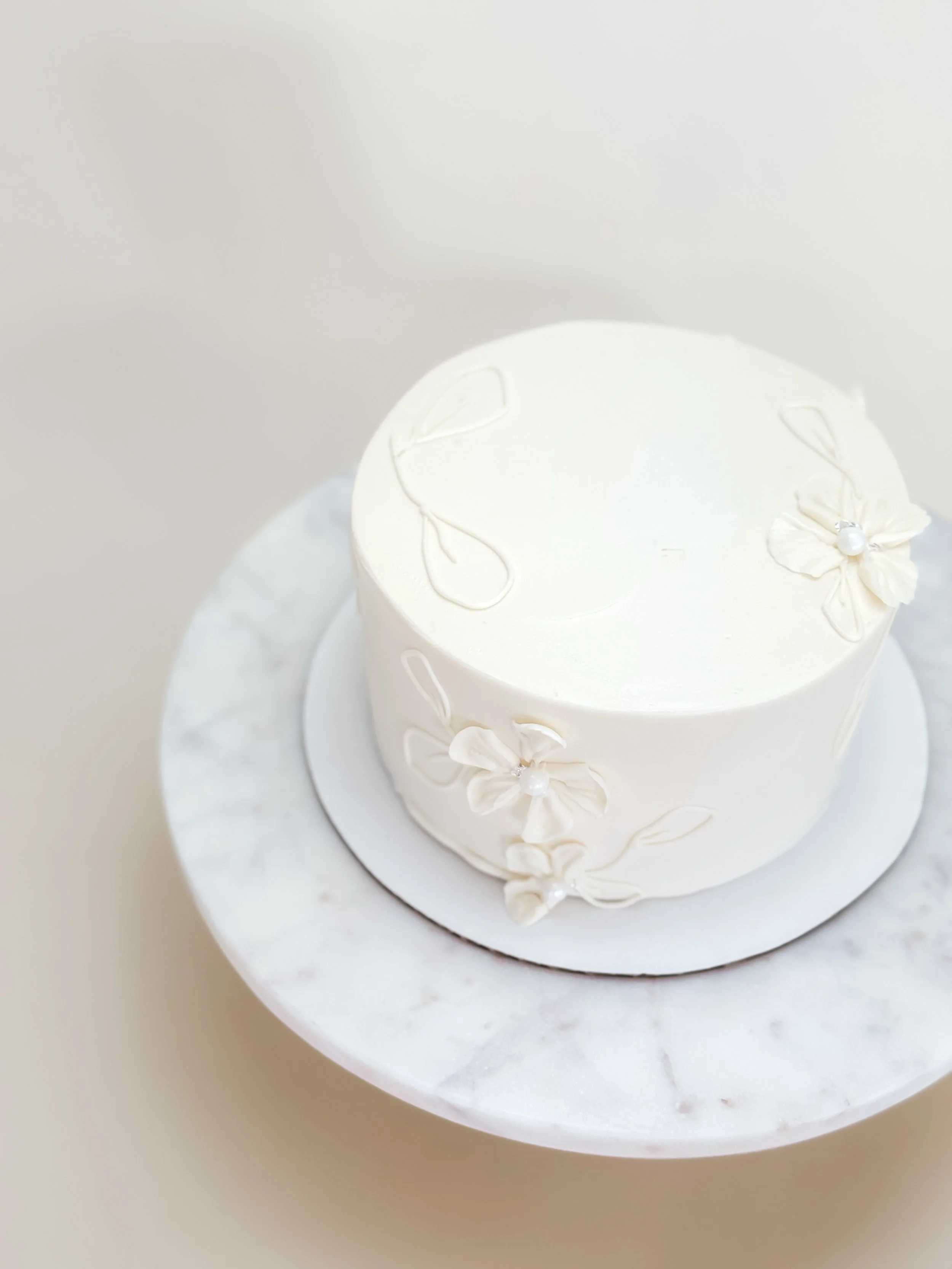 A white frosted cake decorated with delicate white floral designs 