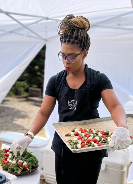 Caterer with black shirt and black apron preparing trays of caprese skewers