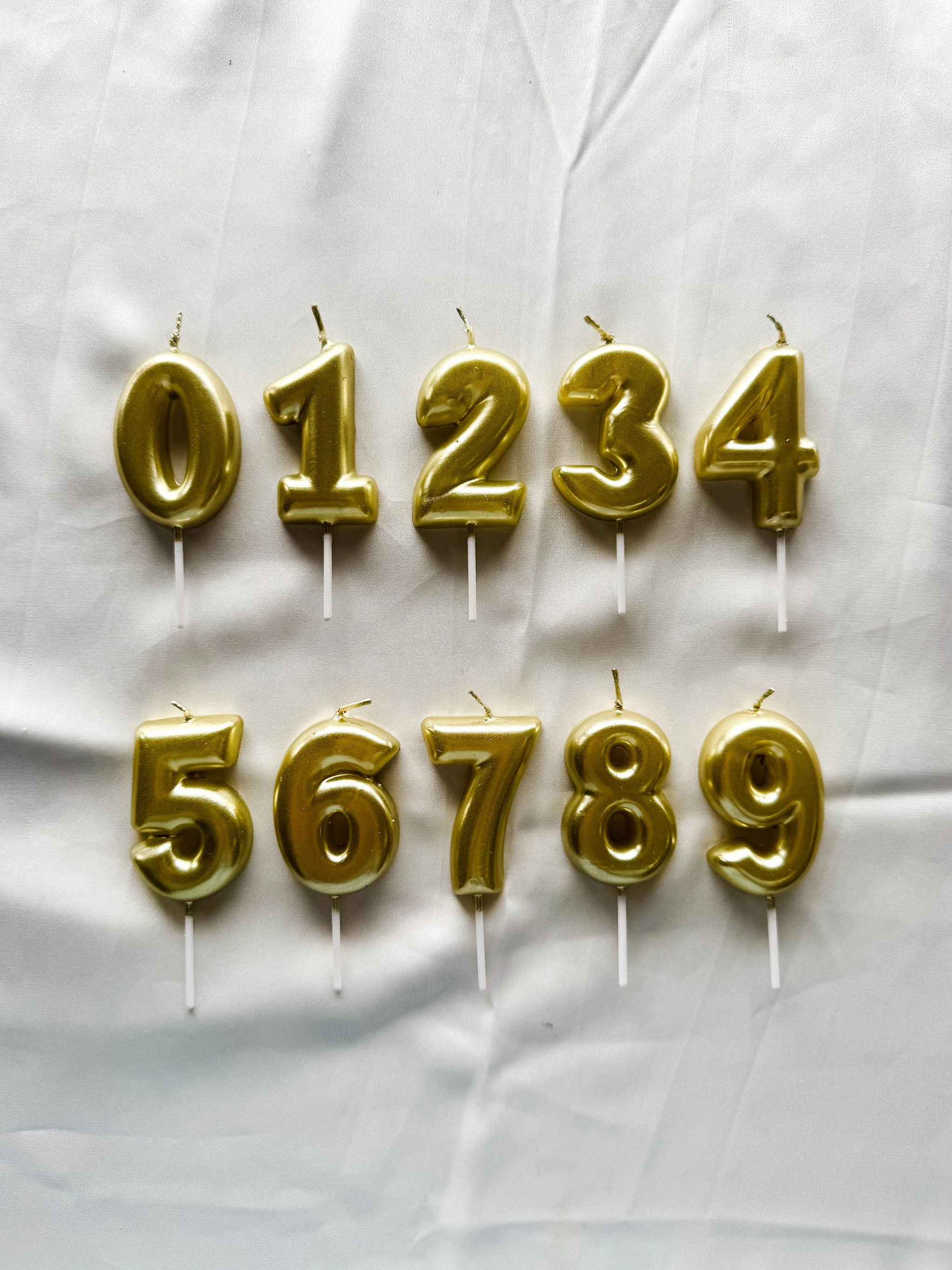 Gold Number Candles 0 through 9 on a white satin cloth background