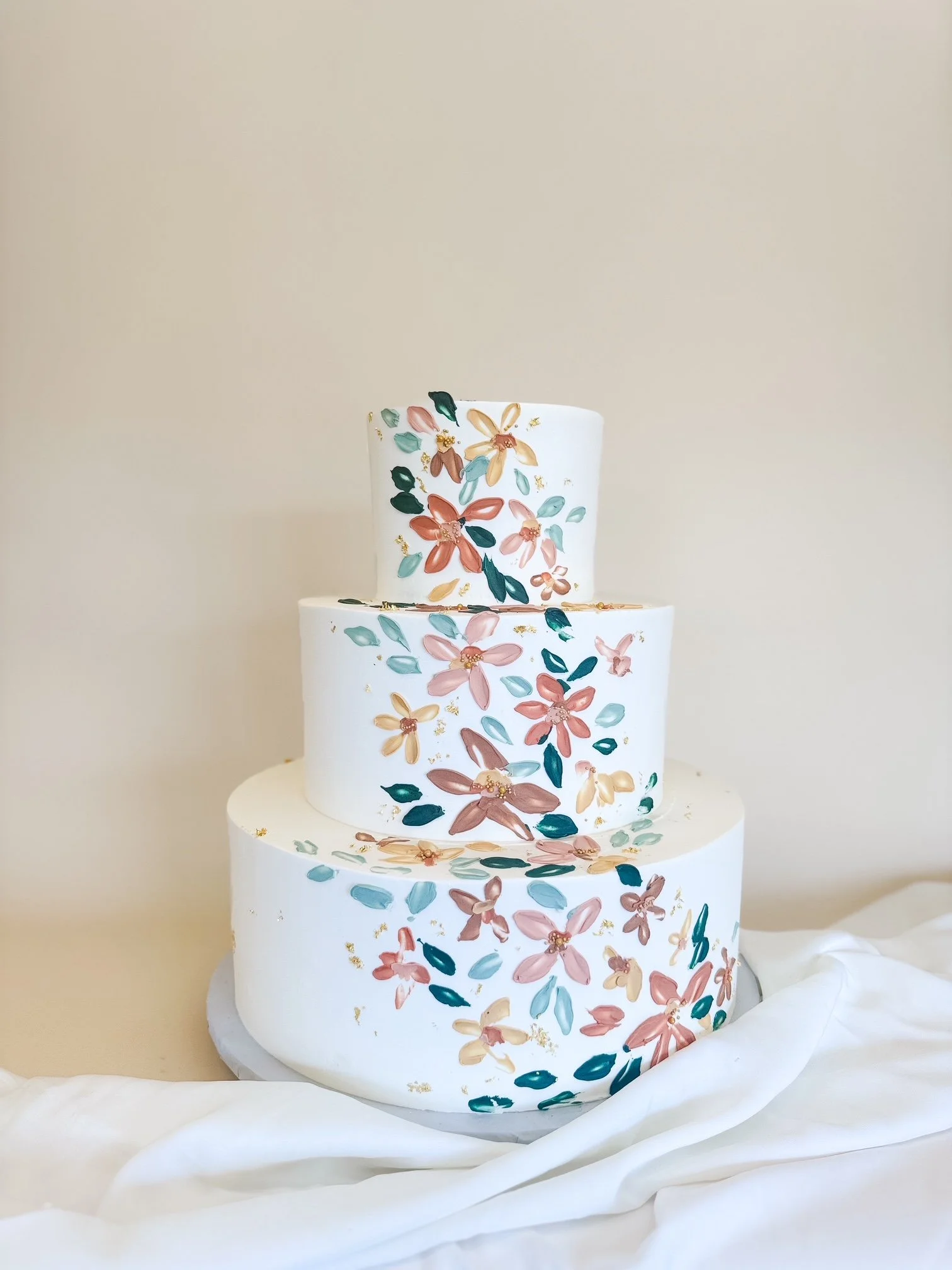 wedding cake with hand-painted floral designs in pink, beige, teal, and gold 