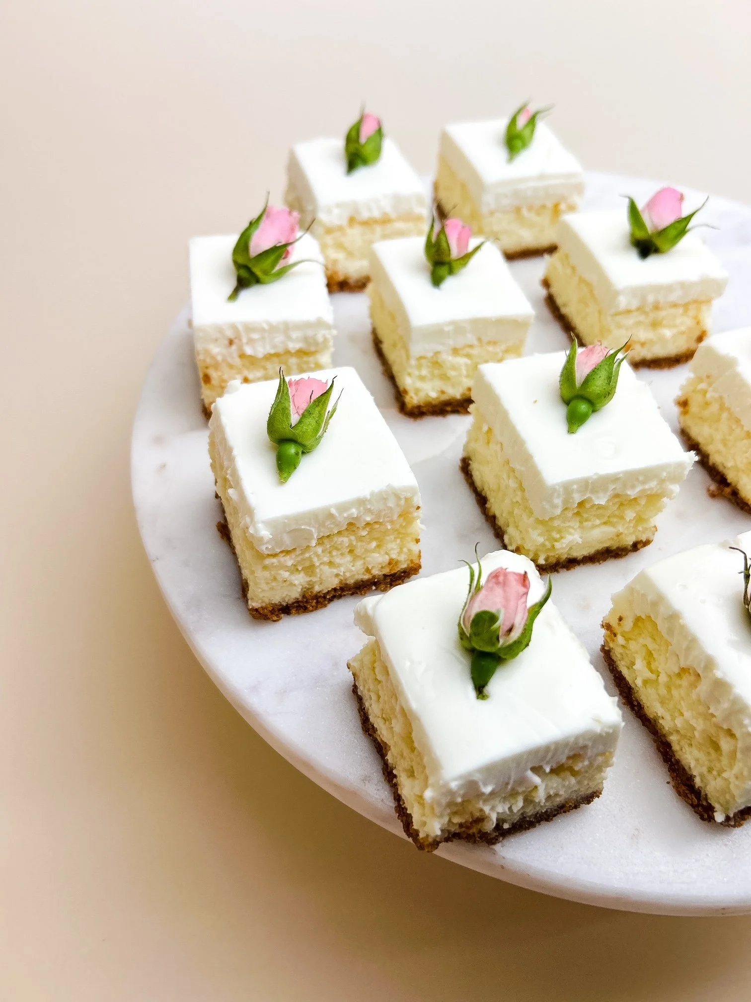 Cheesecake slices with pink rose buds on a white marble platter.