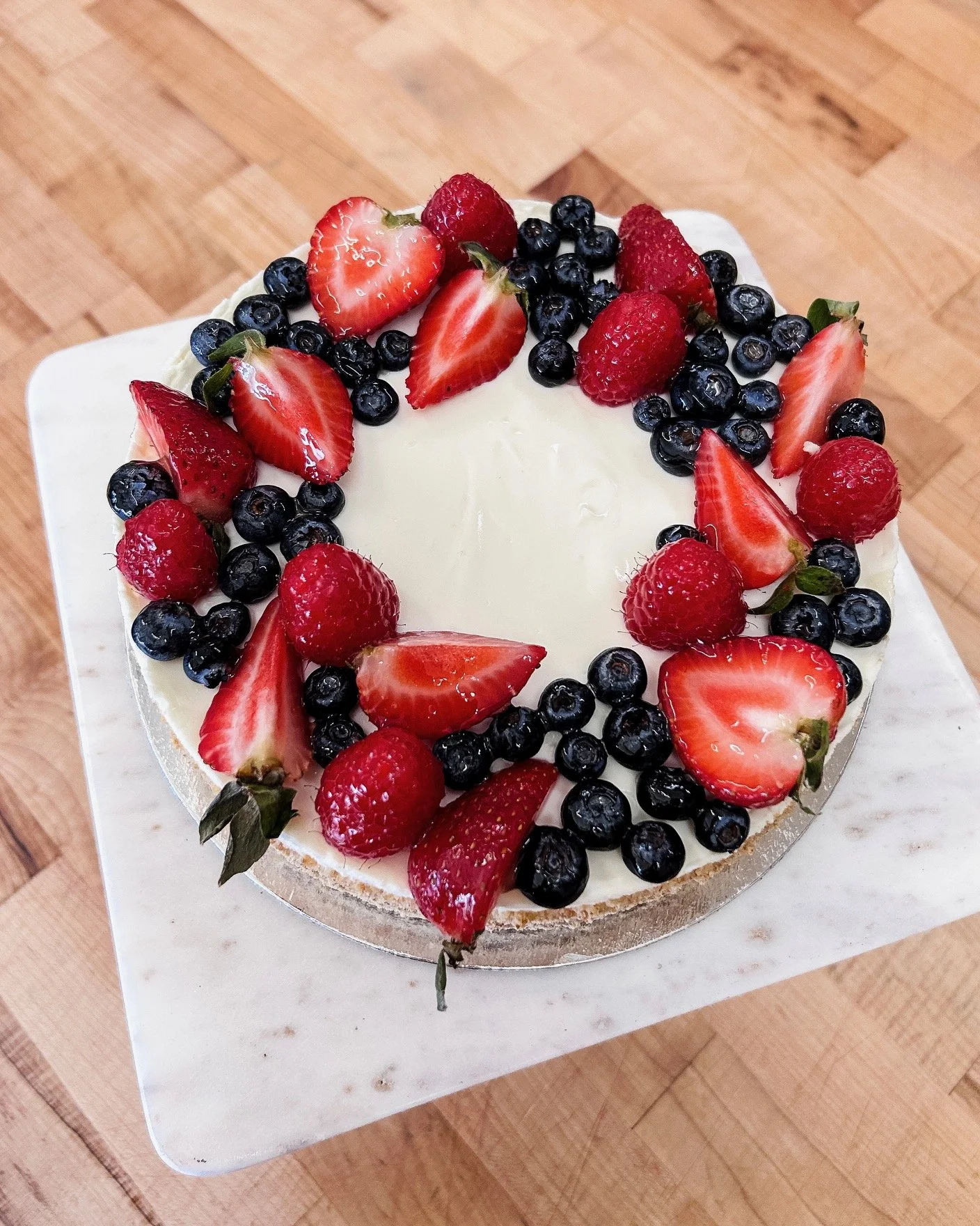 A cheesecake topped with fresh berries on a marble cake stand