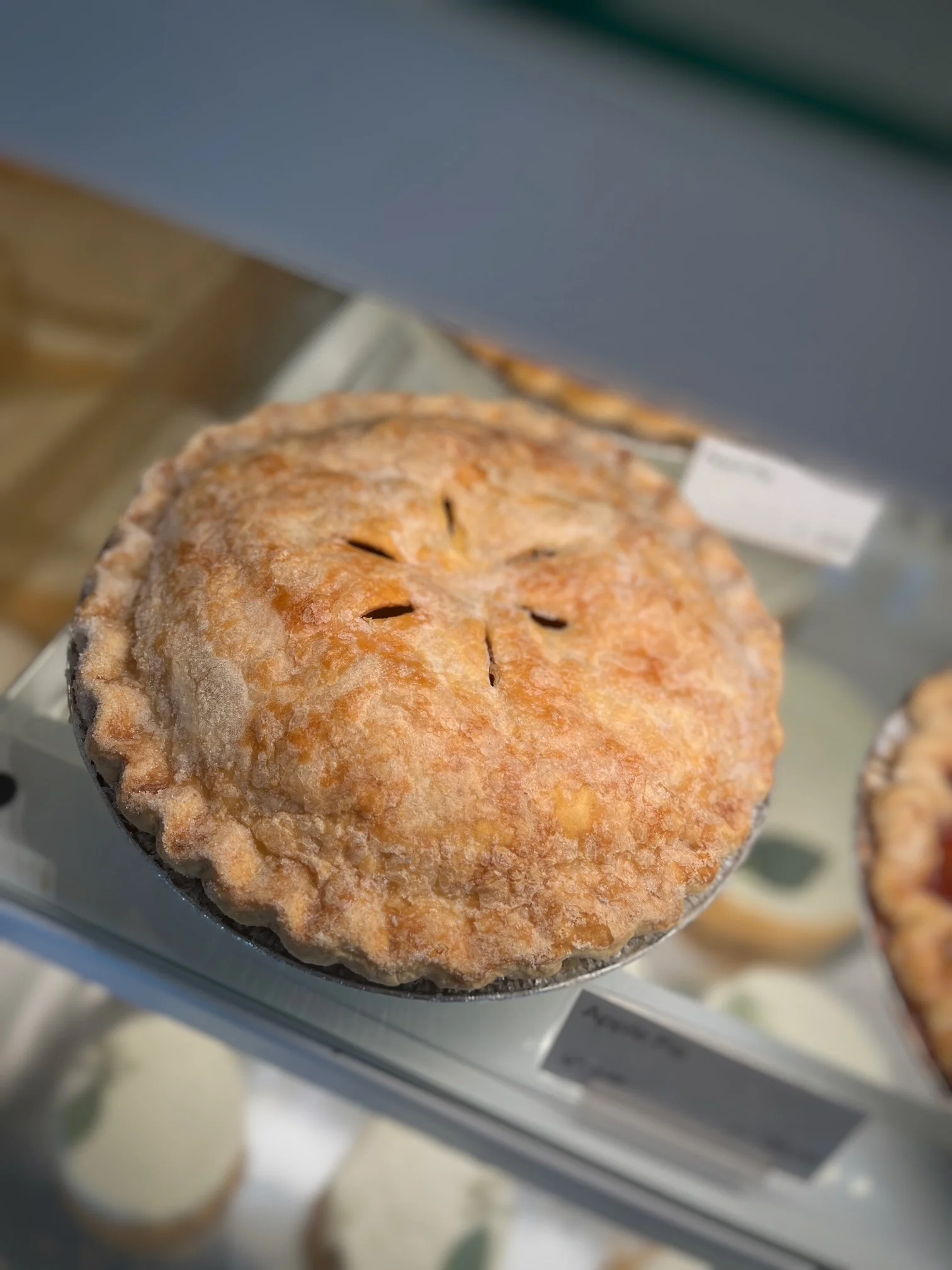 A golden-brown pie with crimped edges displayed on a glass shelf.
