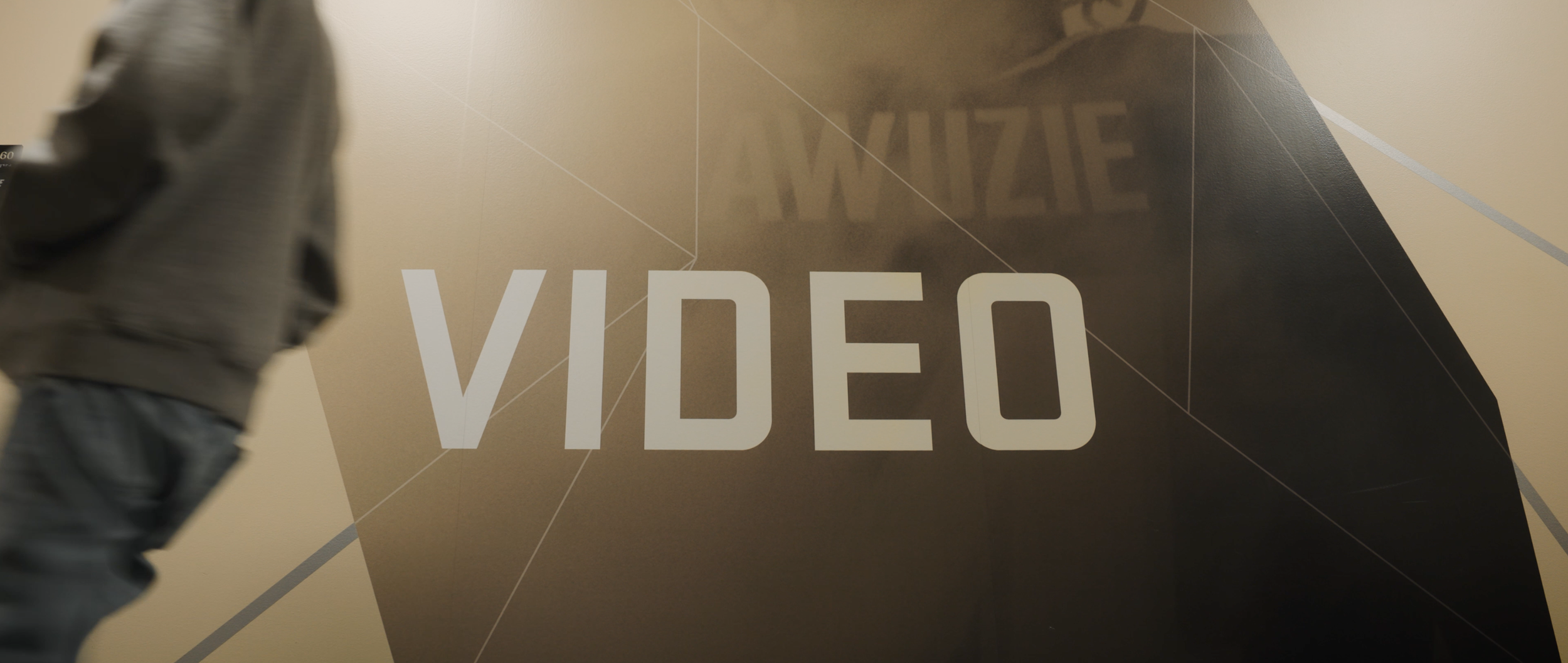 Person walking past a wall with the word "VIDEO" in large white letters, and a geometric background design.
