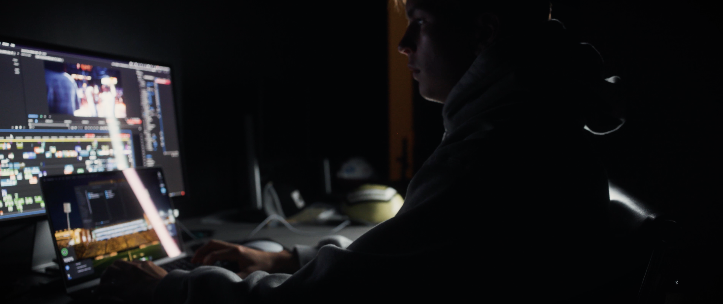 Person working on video editing or graphic design on multiple screens in a dark room.