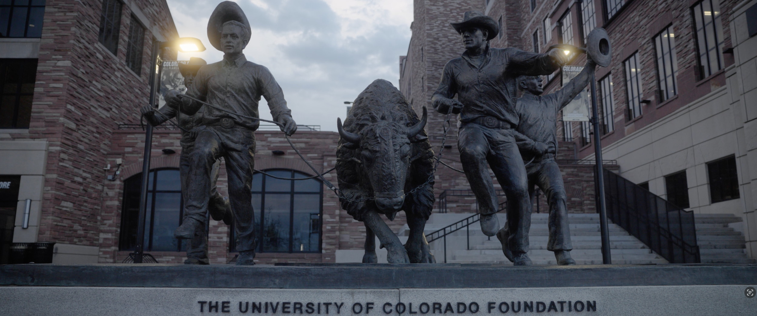 Bronze statue of two cowboys guiding a buffalo, located in front of the University of Colorado Foundation building.