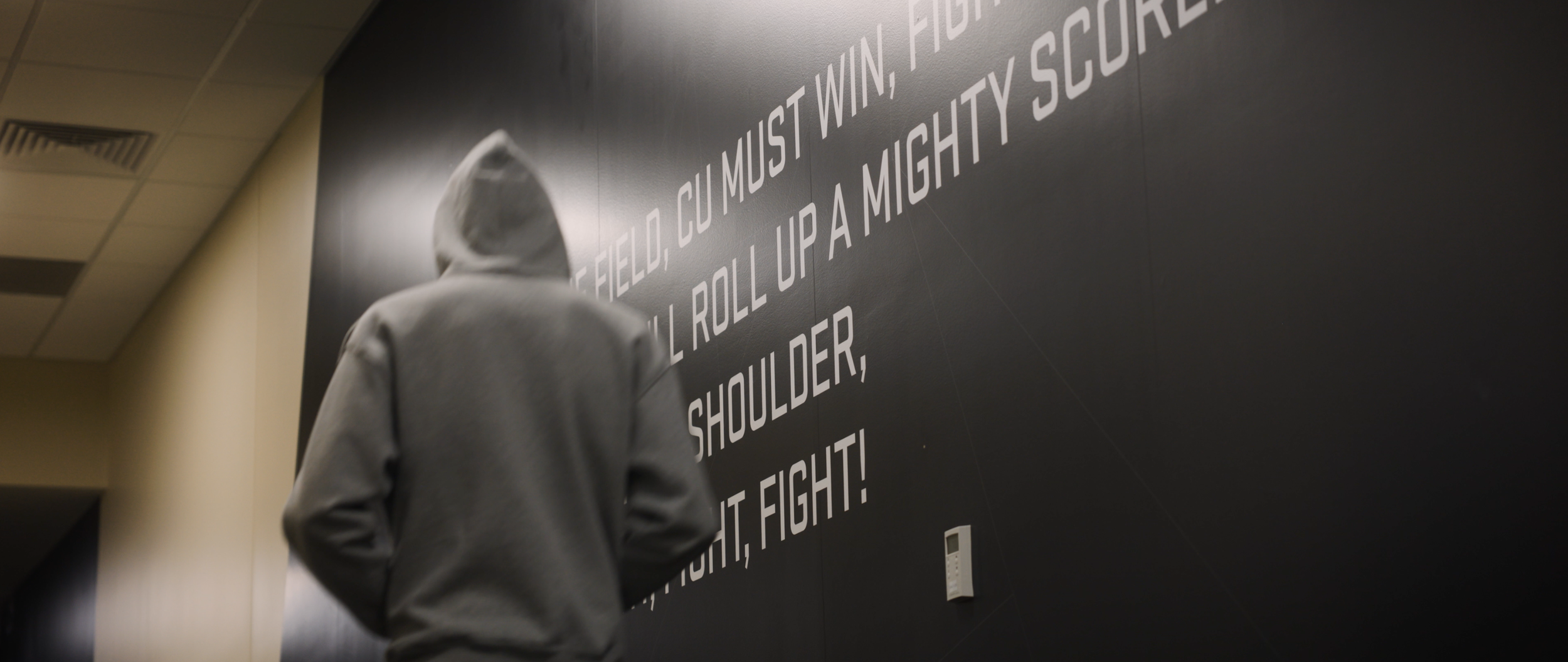 Person wearing a gray hoodie with the hood up, standing in front of a black wall with motivational sports quote in white text.